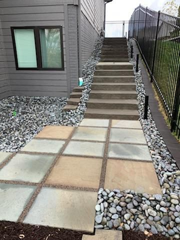 Concrete steps and pathway leading up to a building, flanked by gravel and a black fence.