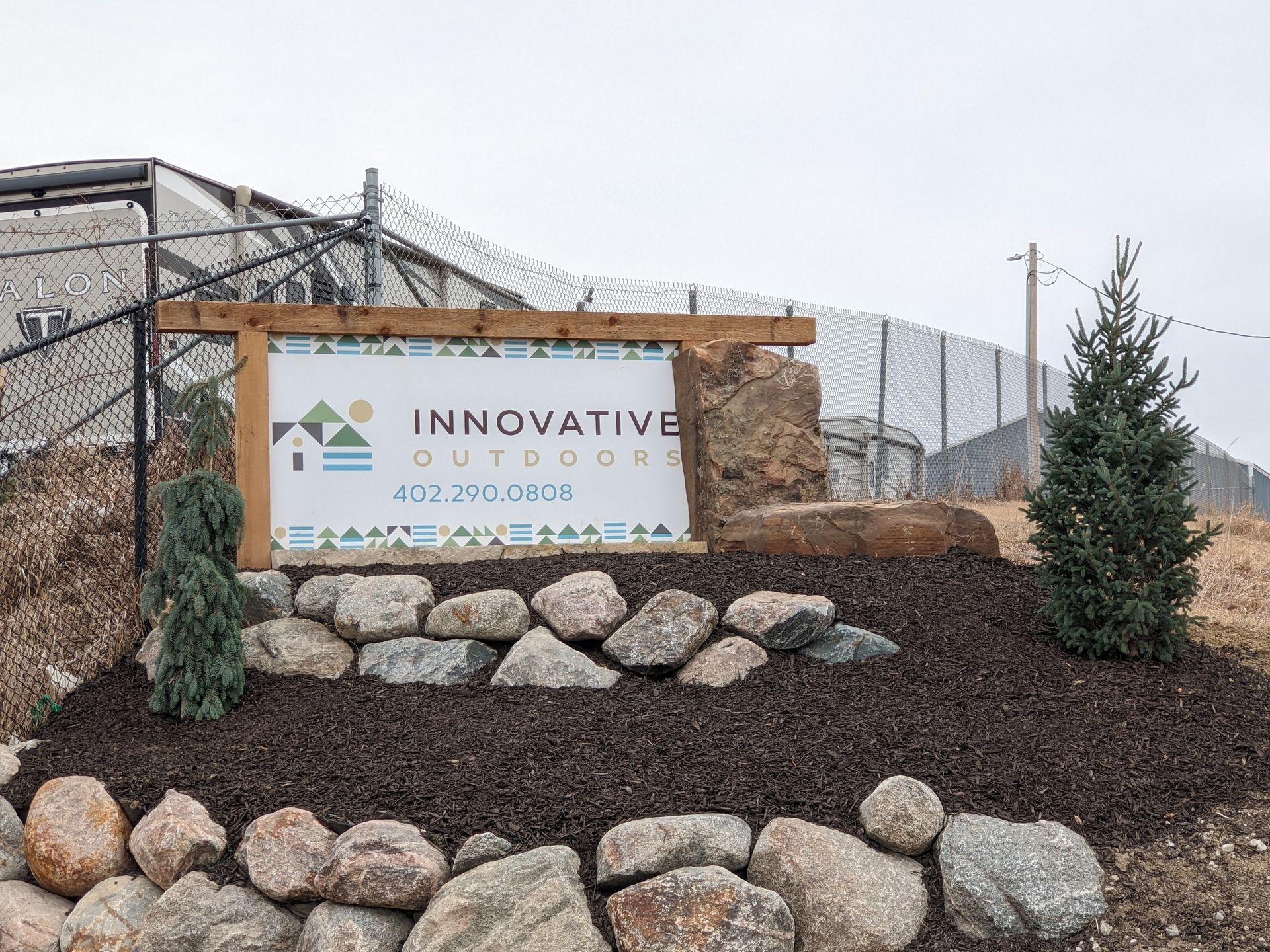 Sign for Innovative Outdoors, with logo, contact info, and decorative rocks in front.