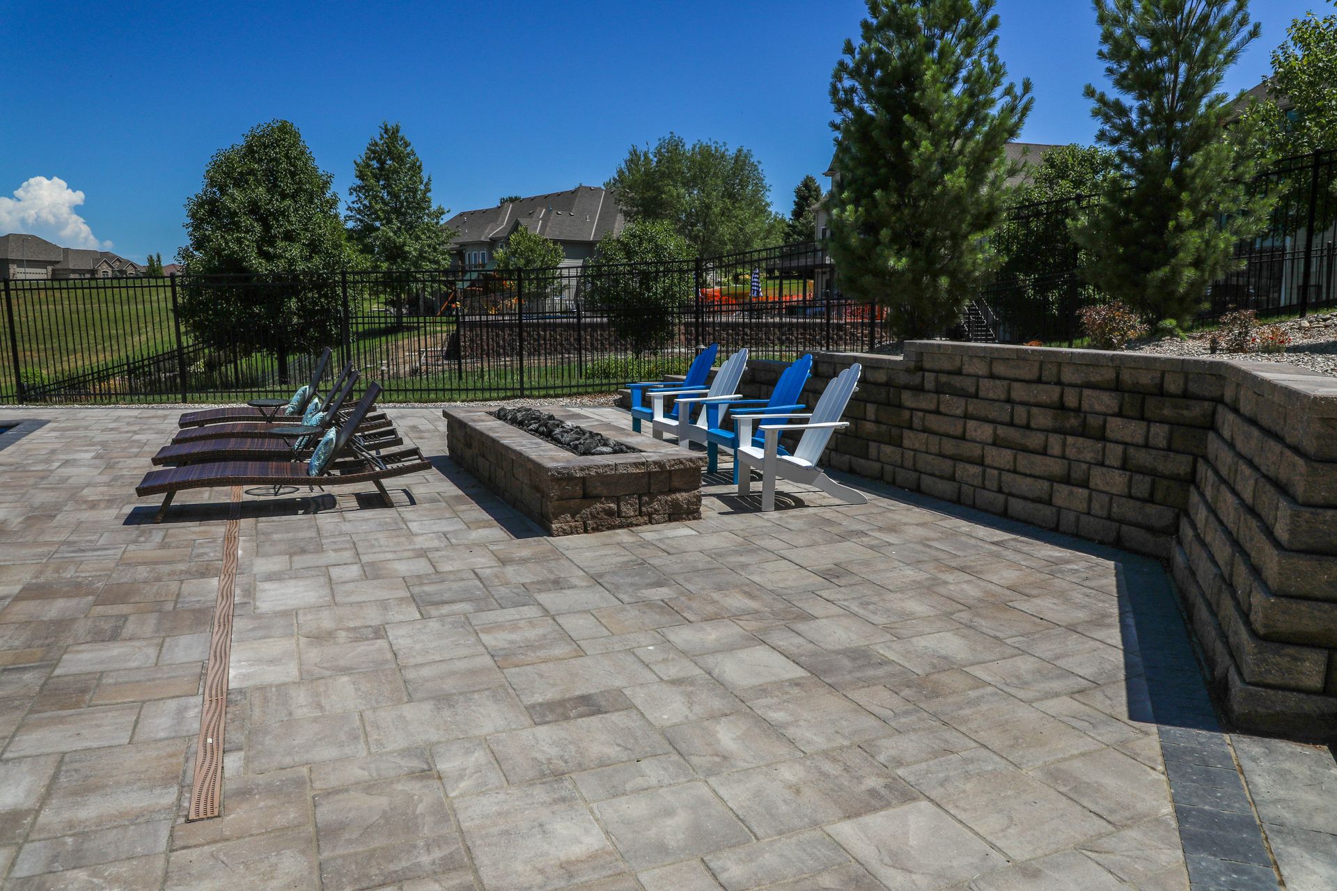 Patio with fire pit, lounge chairs, and stone wall on a sunny day.