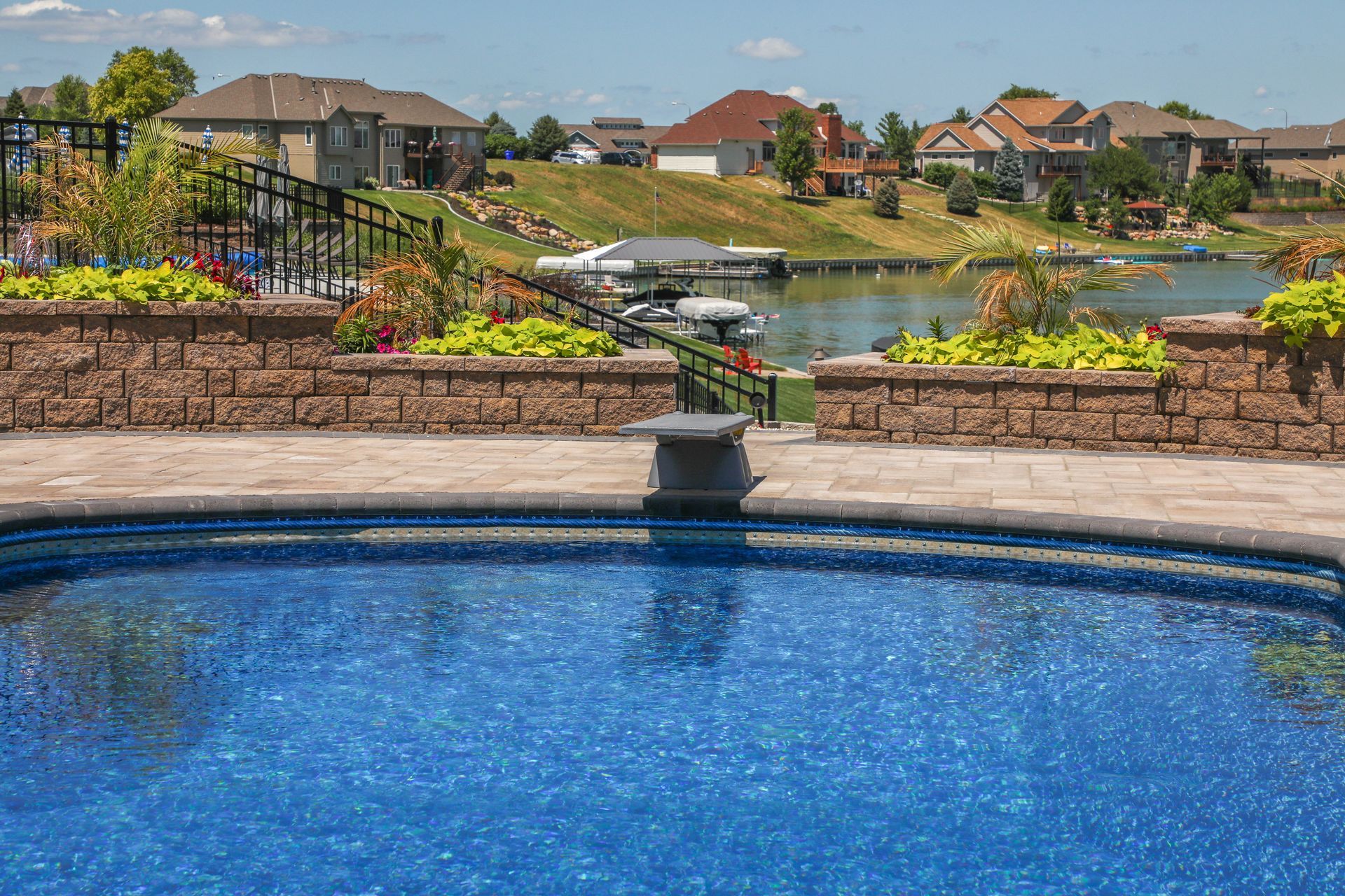 Swimming pool overlooking a lake, with houses in the background on a sunny day.