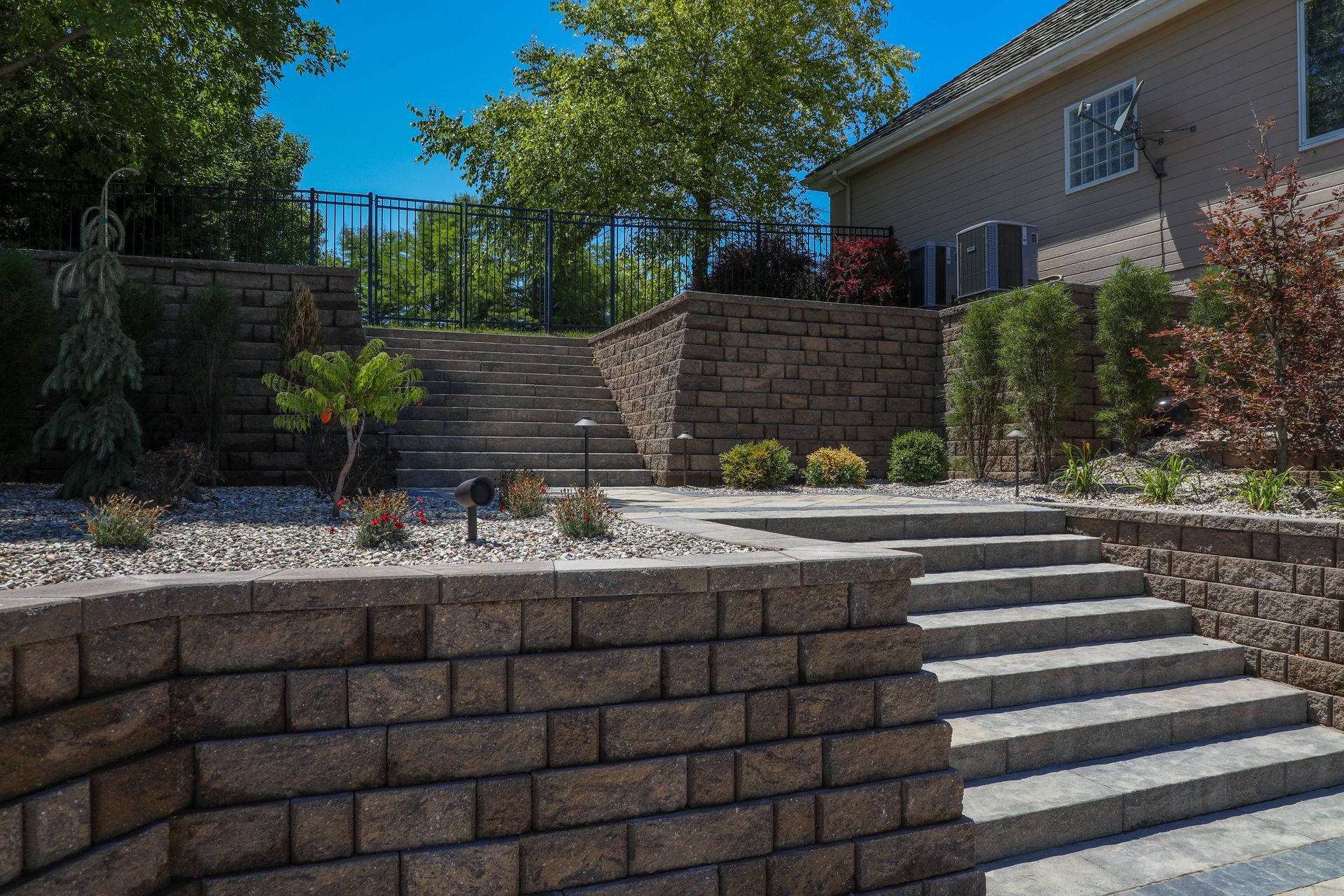 Stone retaining walls with steps leading up to a backyard with trees and a house.