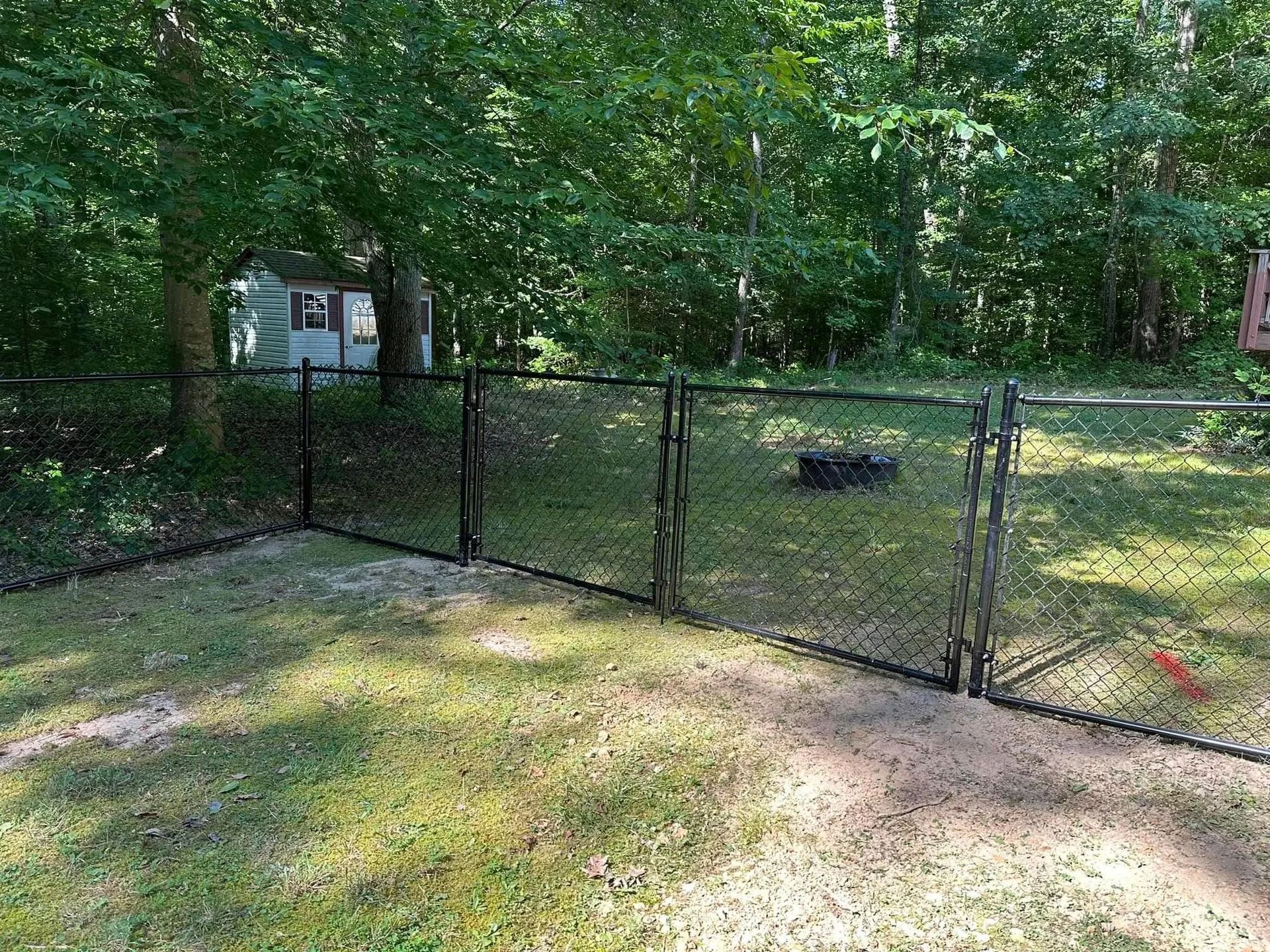 Black chain link fence in a grassy yard, with trees in the background.