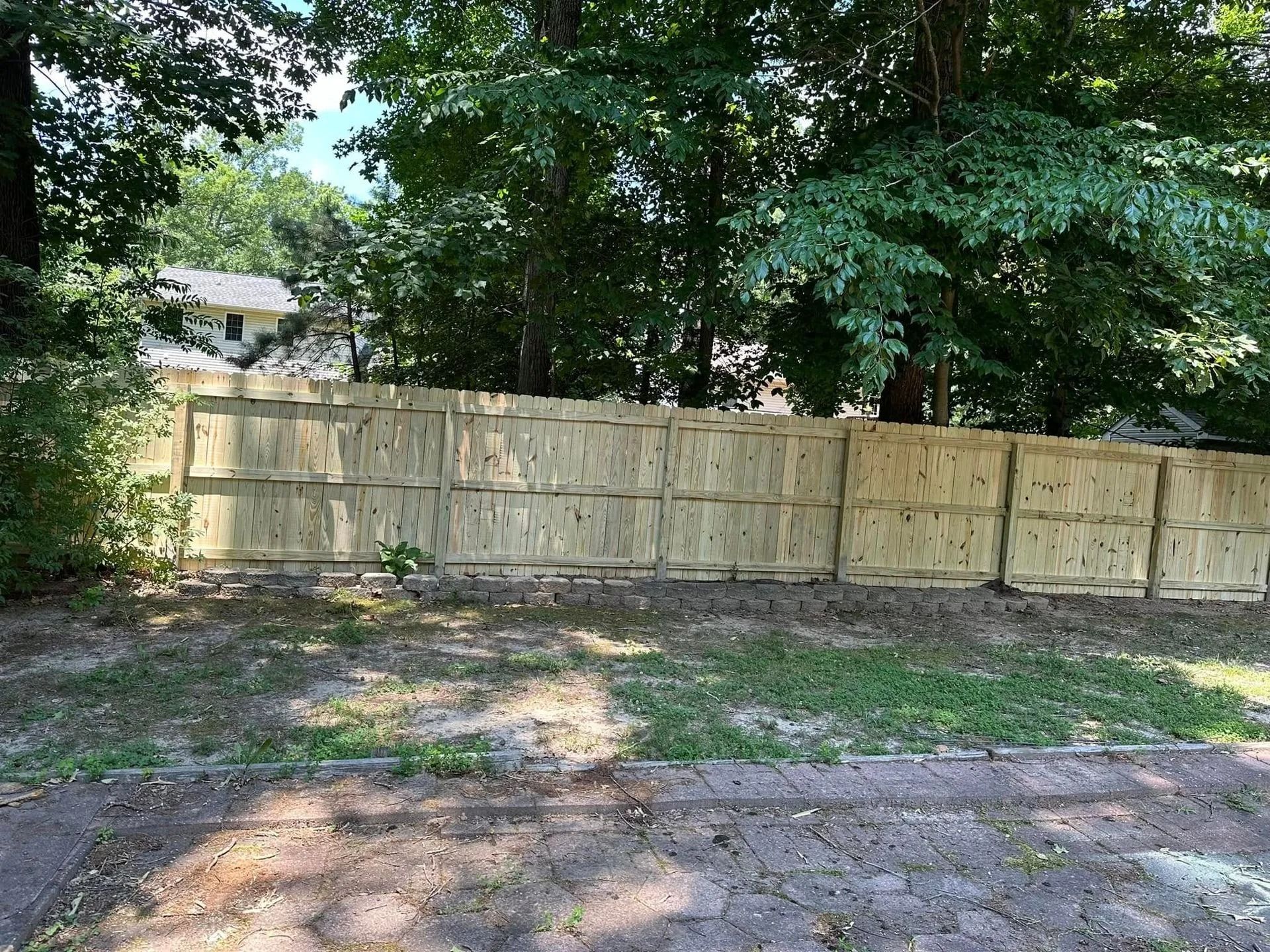 Wooden fence in front of trees, grass in foreground, daytime.