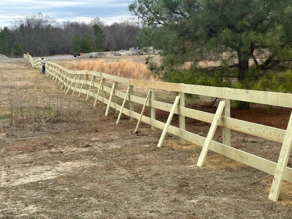 Wooden fence in a field, supported by diagonal braces, with a person in the distance.