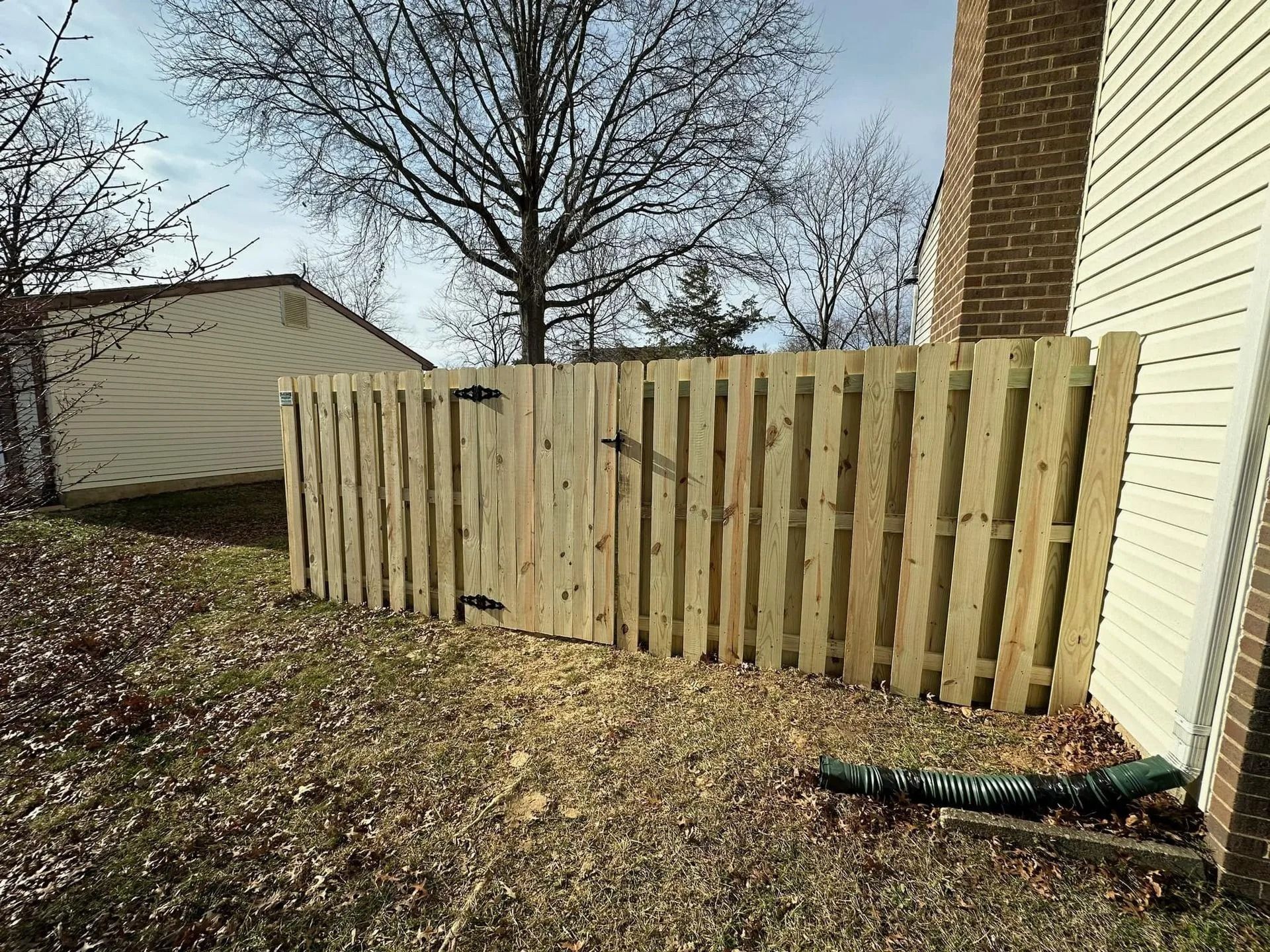 Wooden fence with gate, set against a building and leafless trees.