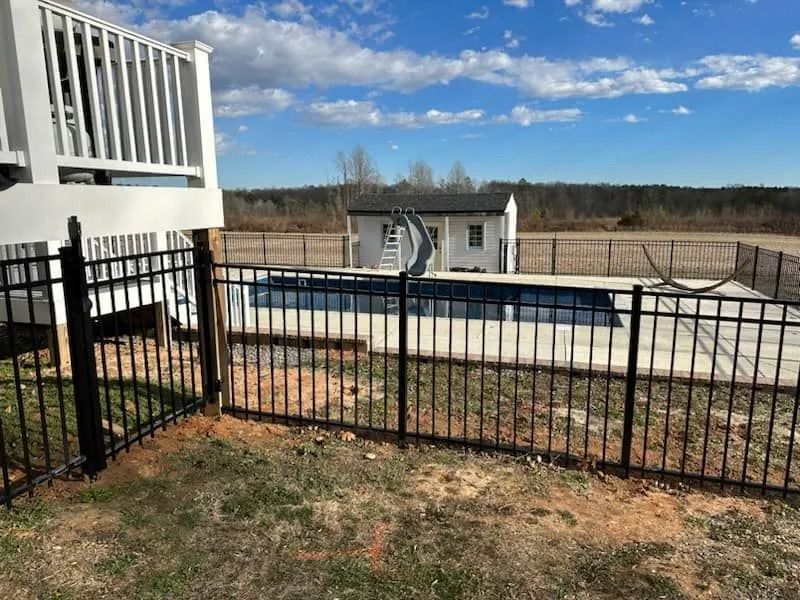 Black fence surrounds a rectangular pool, white shed in background, deck on left, blue sky.