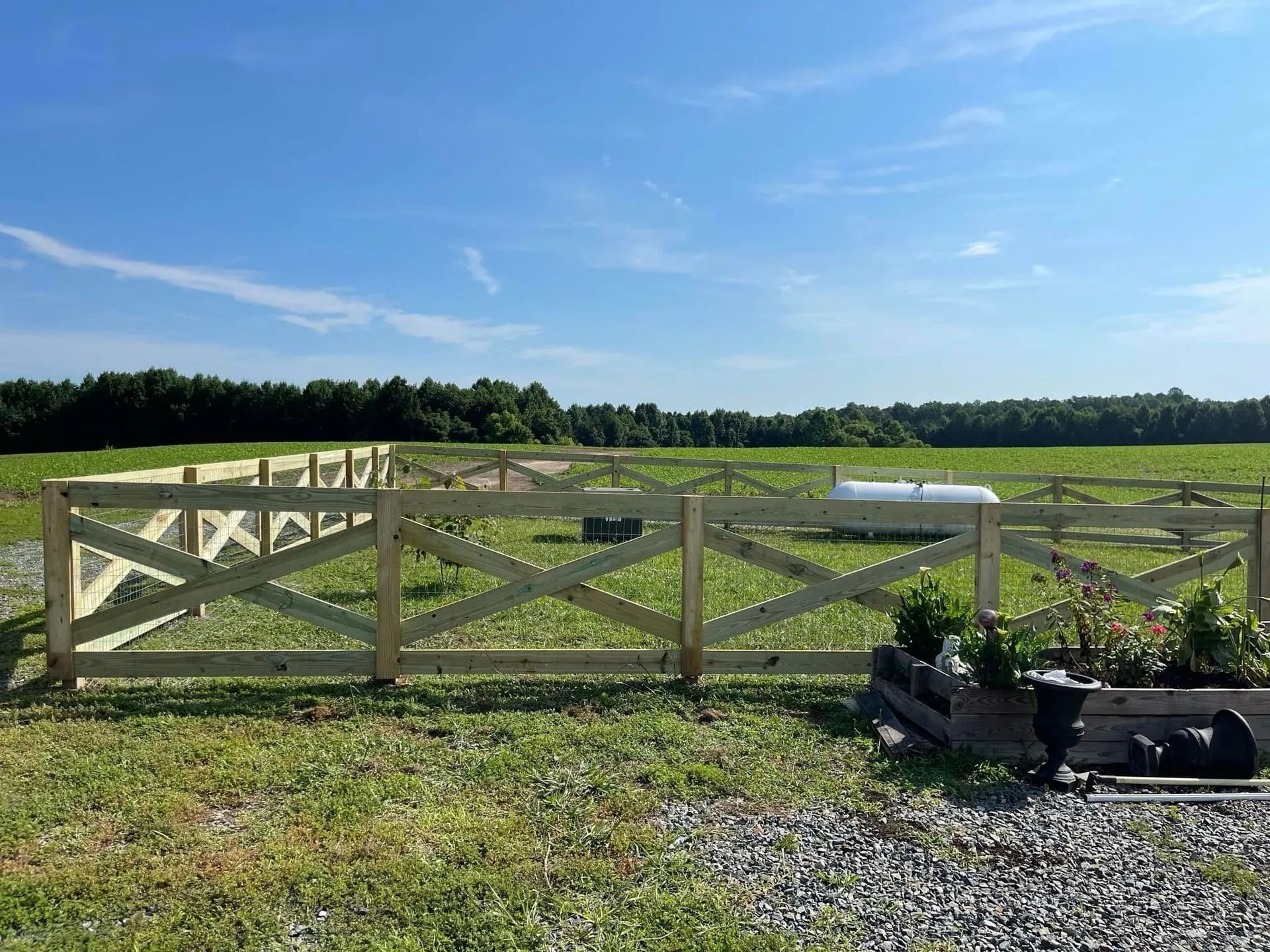 Wooden fence around a garden in a field on a sunny day.