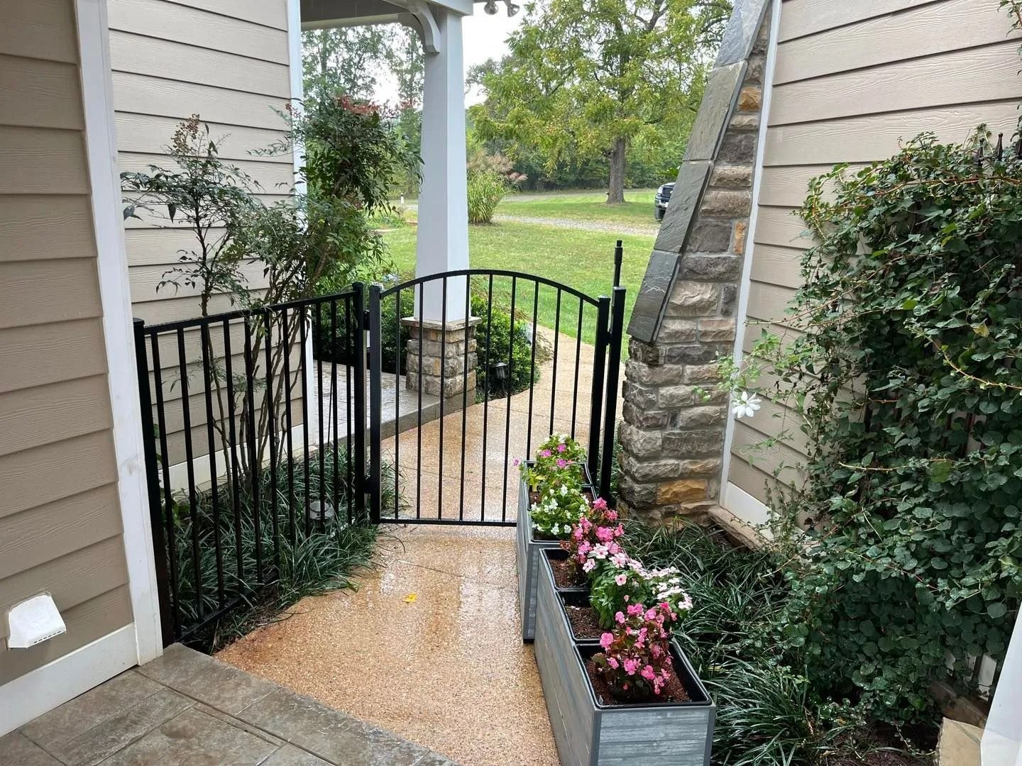 Black gate in a small entry garden with stone walkway and colorful flowers.