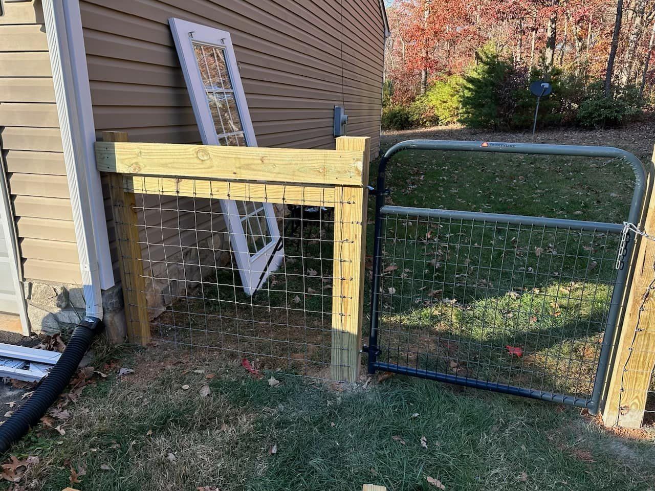 Wooden fence with gate, chicken wire, and a discarded white door against a house.