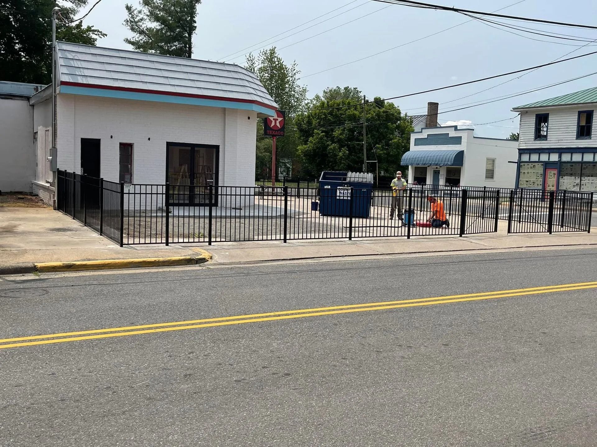 Small white building with black fence and double yellow road lines in the foreground.