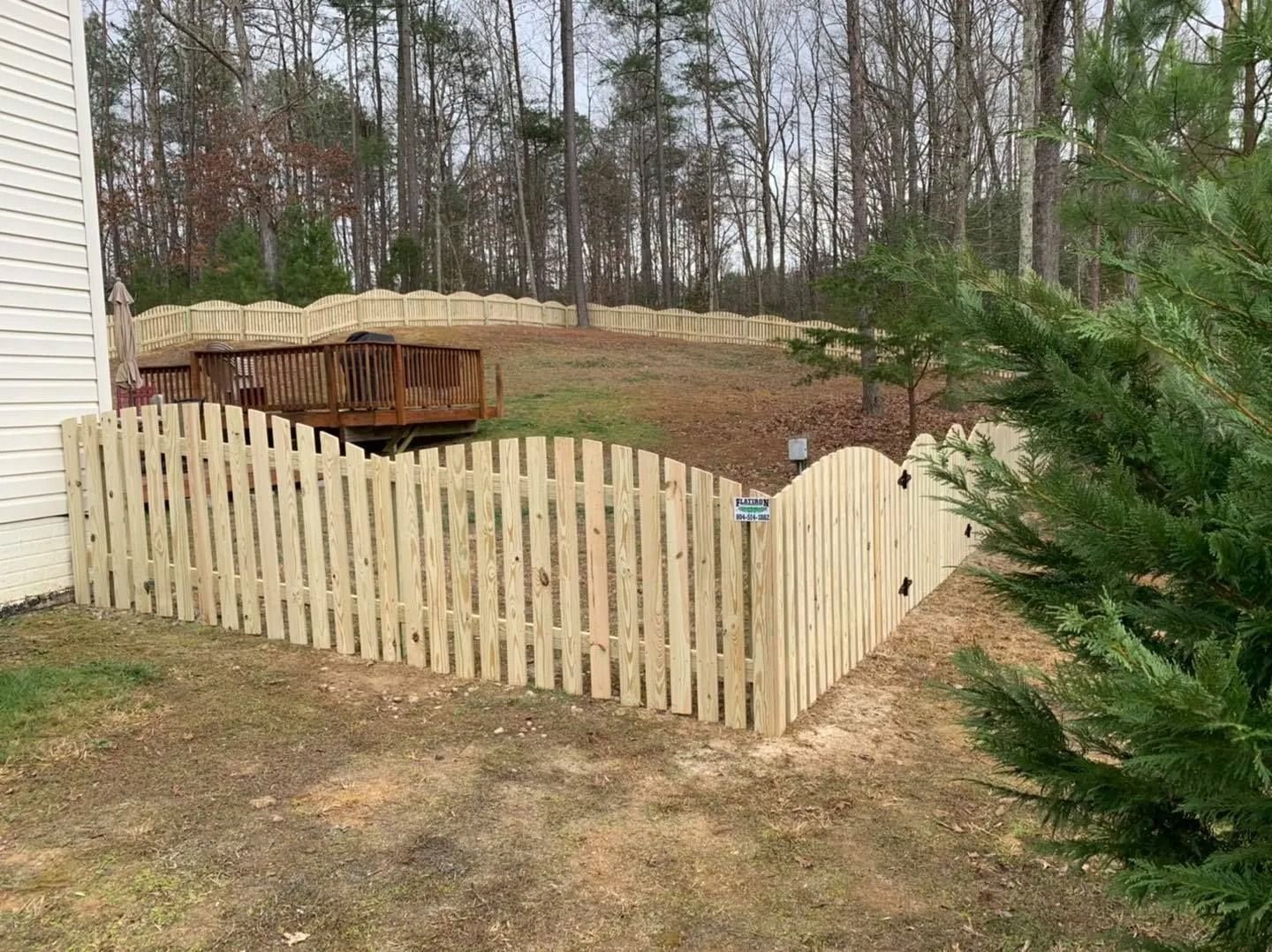 Wooden fence around a grassy backyard with a deck. Trees in the background.