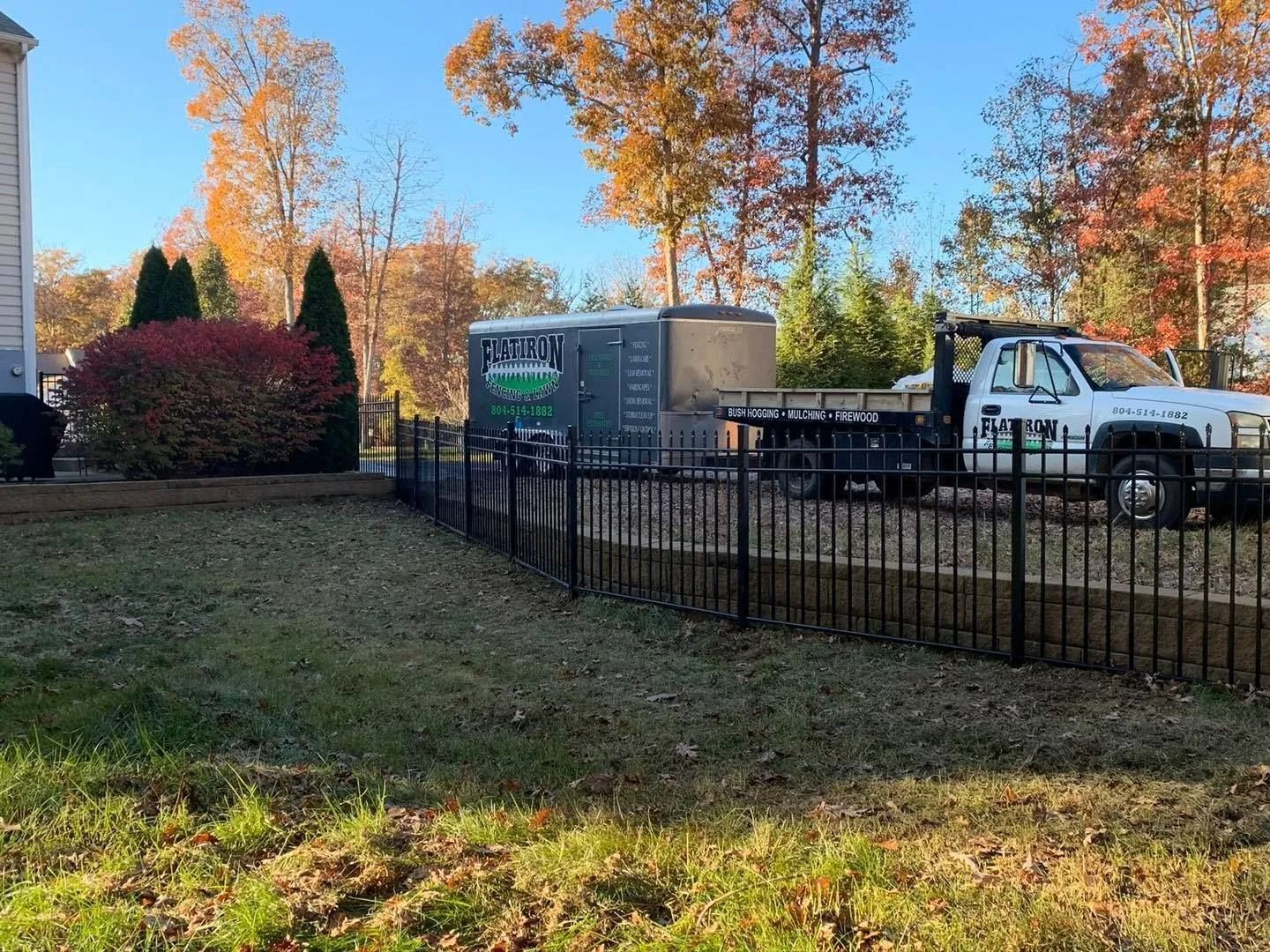 Black metal fence in front yard with a trailer and truck in the background. Fall foliage in the background.