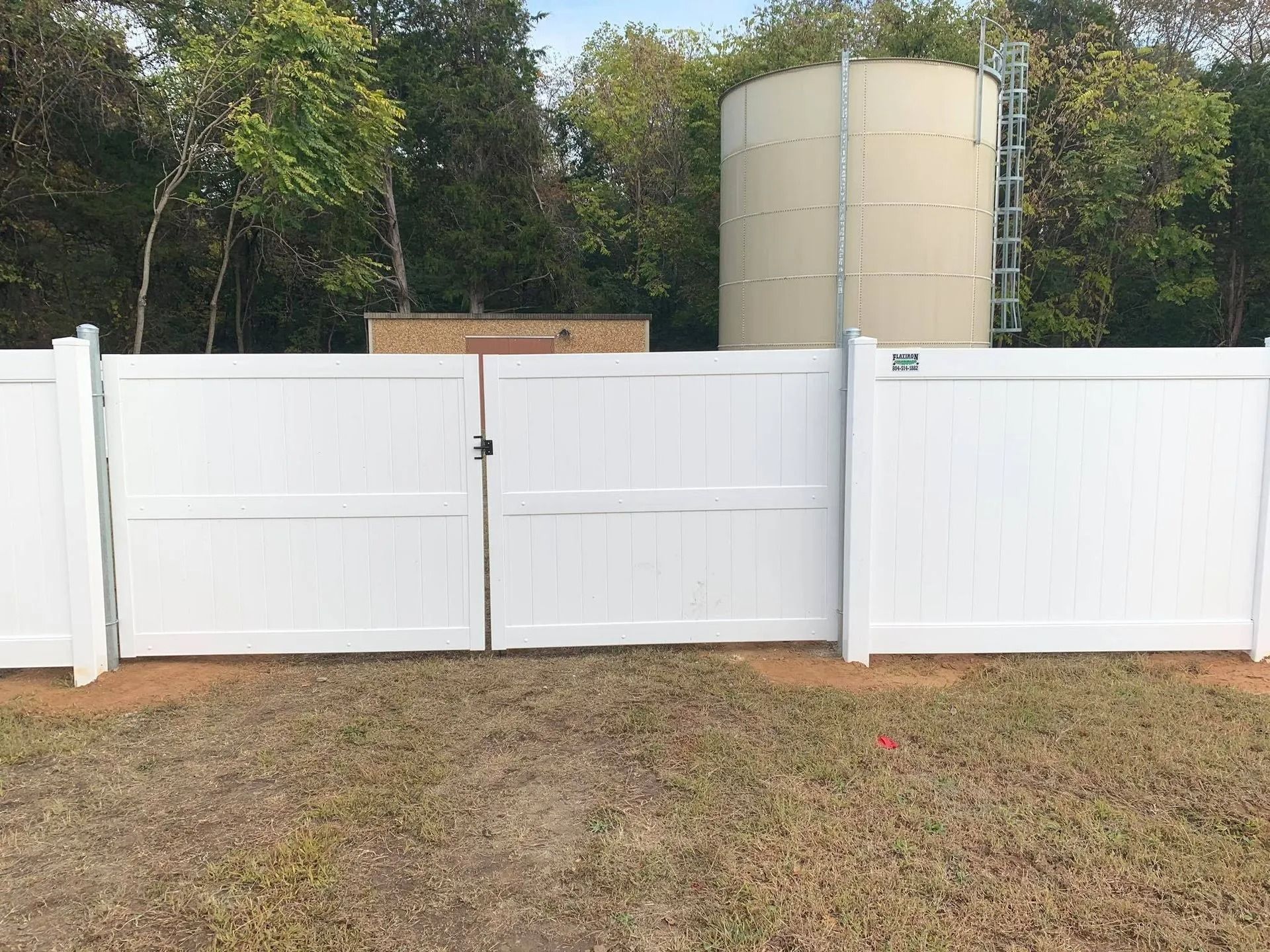 White vinyl fence with gate, behind it is a water tower and trees.