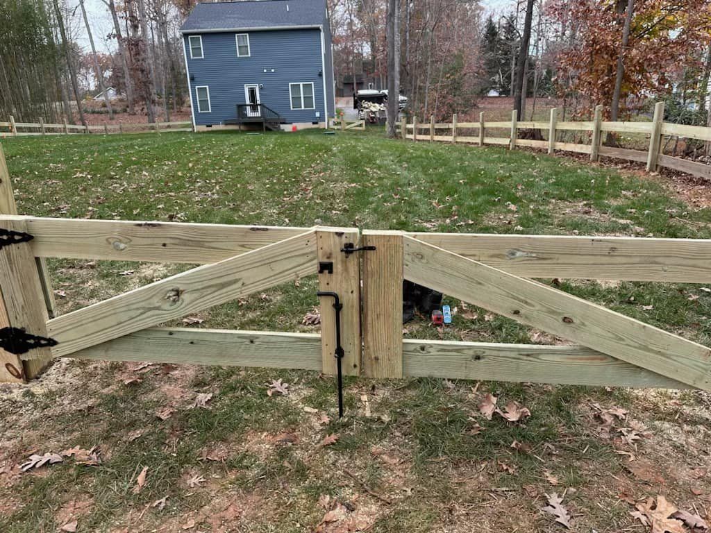 Wooden gate in a split-rail fence; a house is visible in the background.