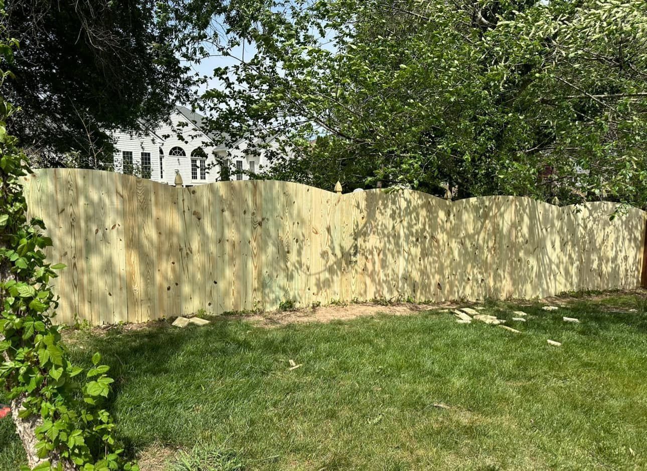 Wooden fence in a yard with green grass and trees in the background.