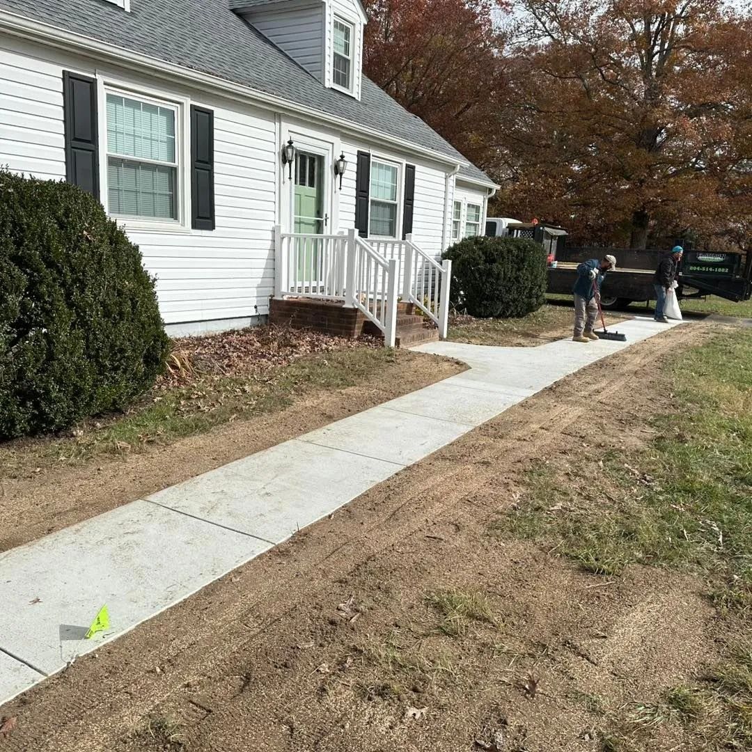White house with a concrete walkway. Two people work near a parked truck on a sunny day.
