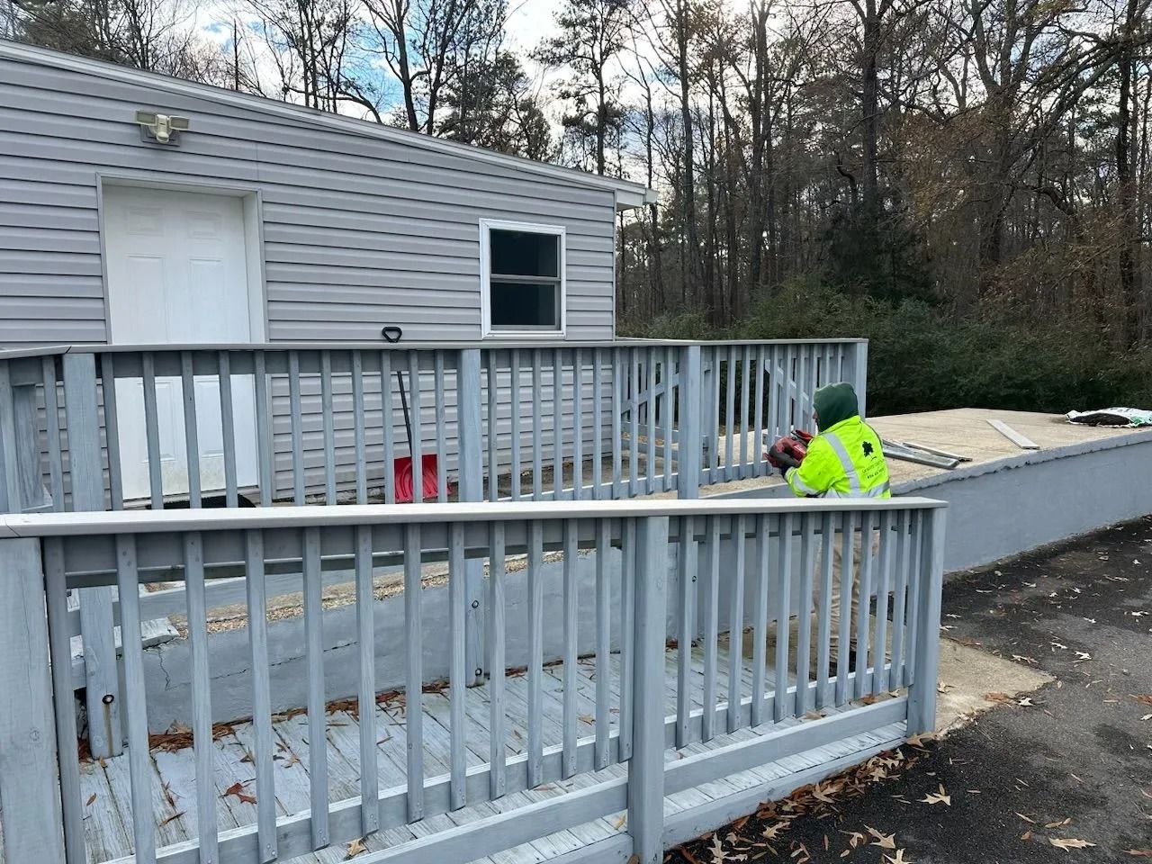 A gray deck with a ramp leads to a building. A person in a neon vest works near a wall.