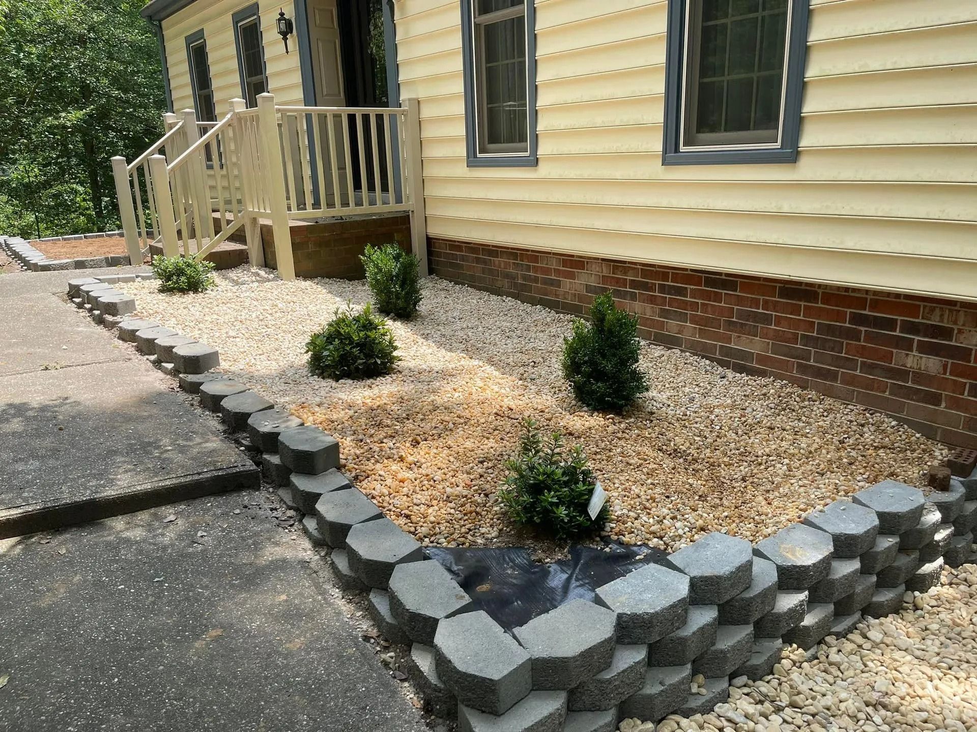 Front yard landscaping with stone retaining wall, shrubs, gravel, and siding.