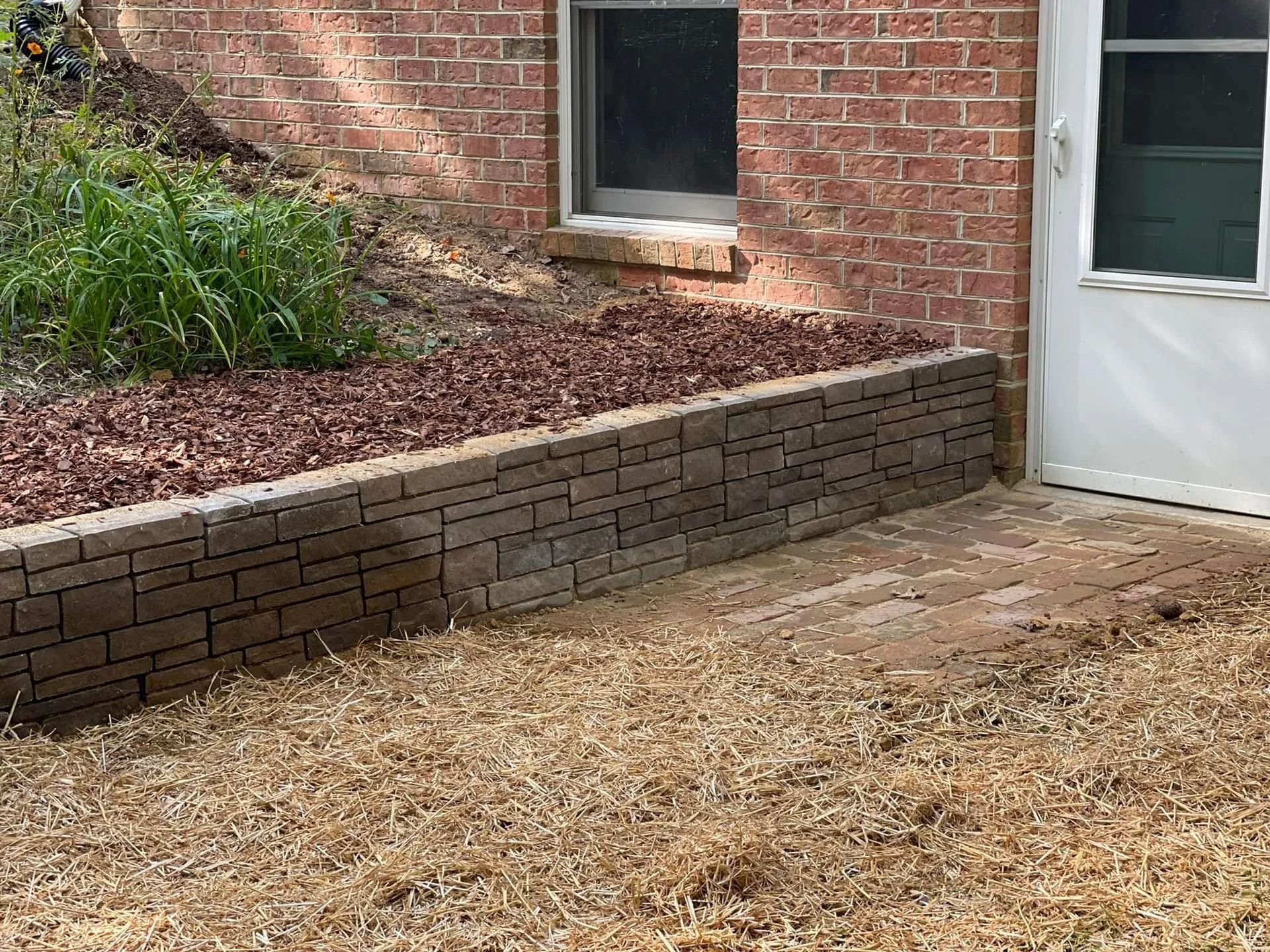 Brick retaining wall with mulch and plants next to a brick building and door.
