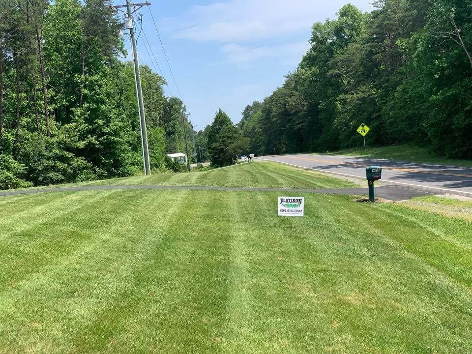 Green, freshly mowed lawn with stripes; road on right, trees on both sides; blue sky.