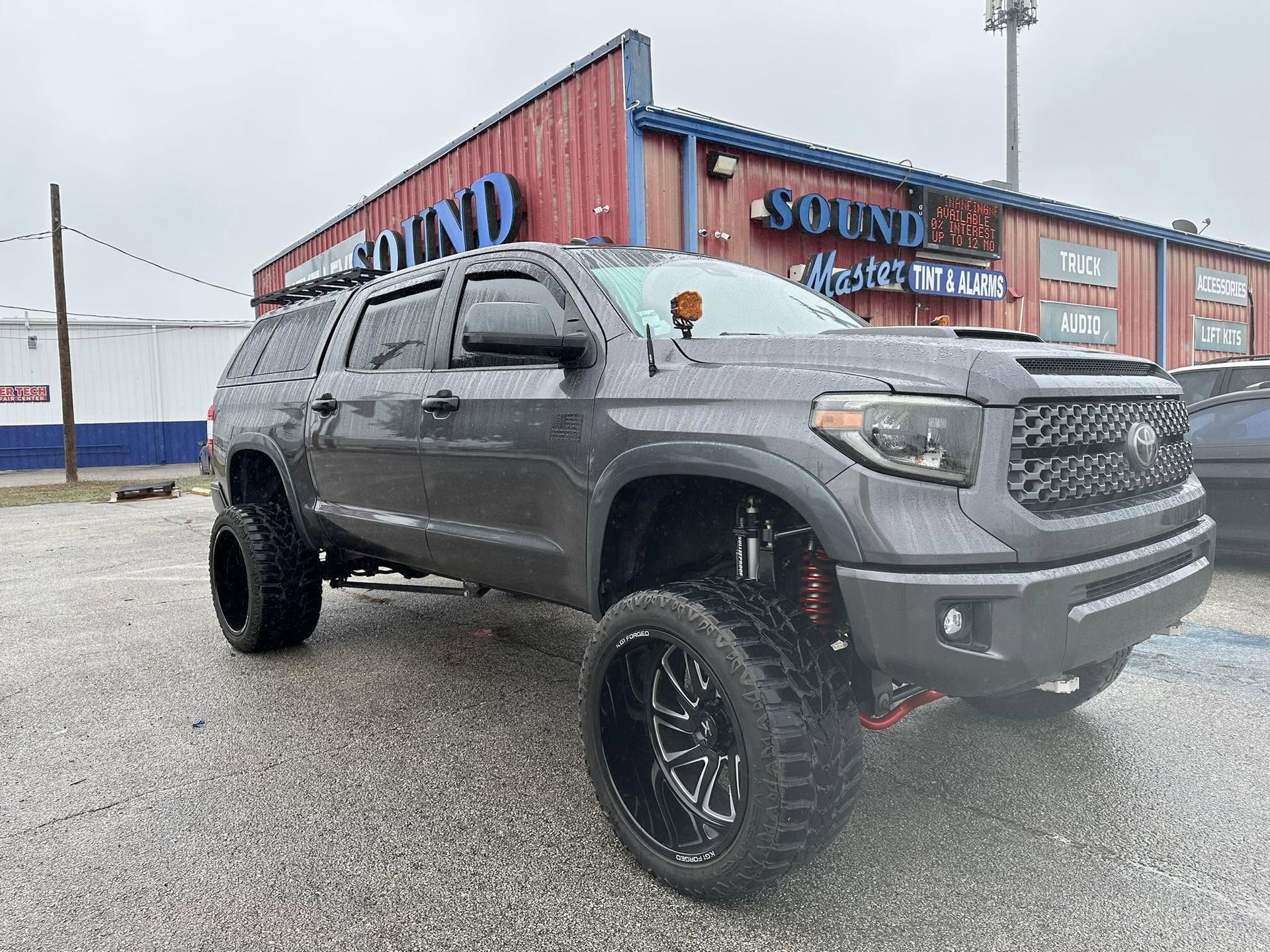 Gray lifted Toyota Tacoma parked outside a Sound Auto building on a wet lot