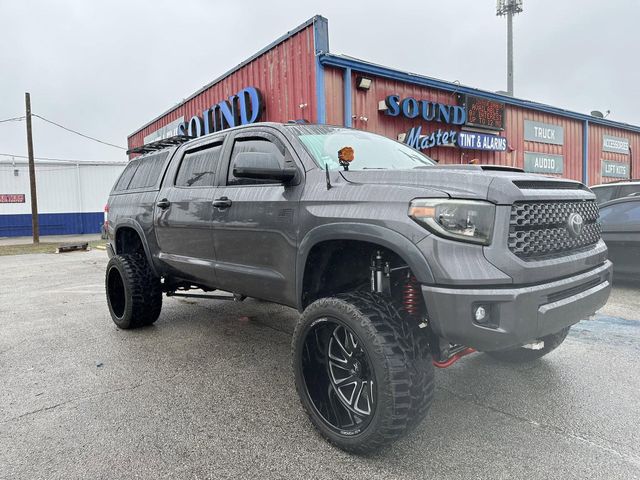 Gray lifted pickup truck parked outside a red Sound building on a wet gravel lot