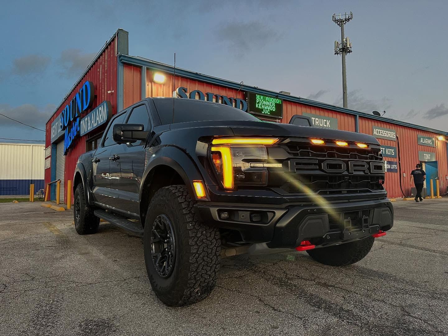 Black pickup truck parked beside a colorful industrial building at dusk