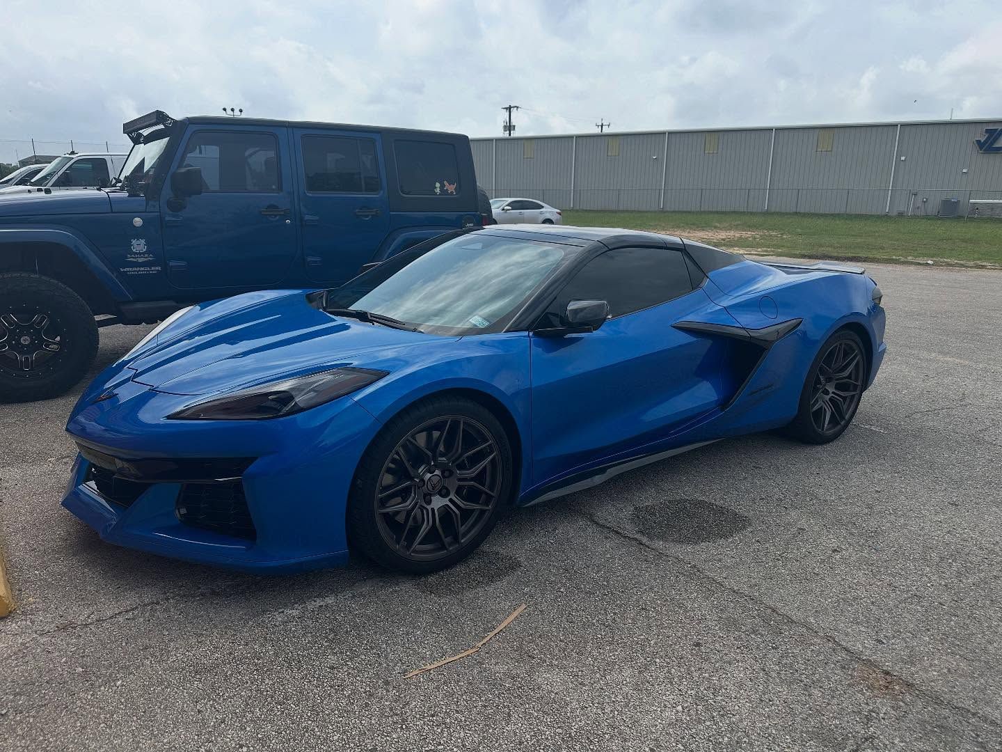 Blue sports car parked on asphalt beside a black SUV in an industrial lot