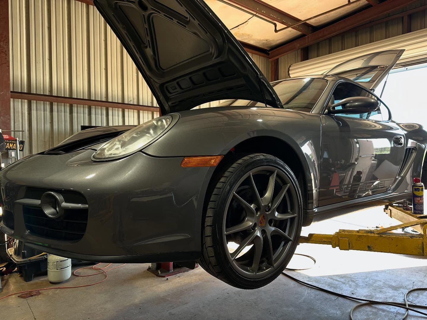Gray sports car on a lift in a garage with its hood open during maintenance