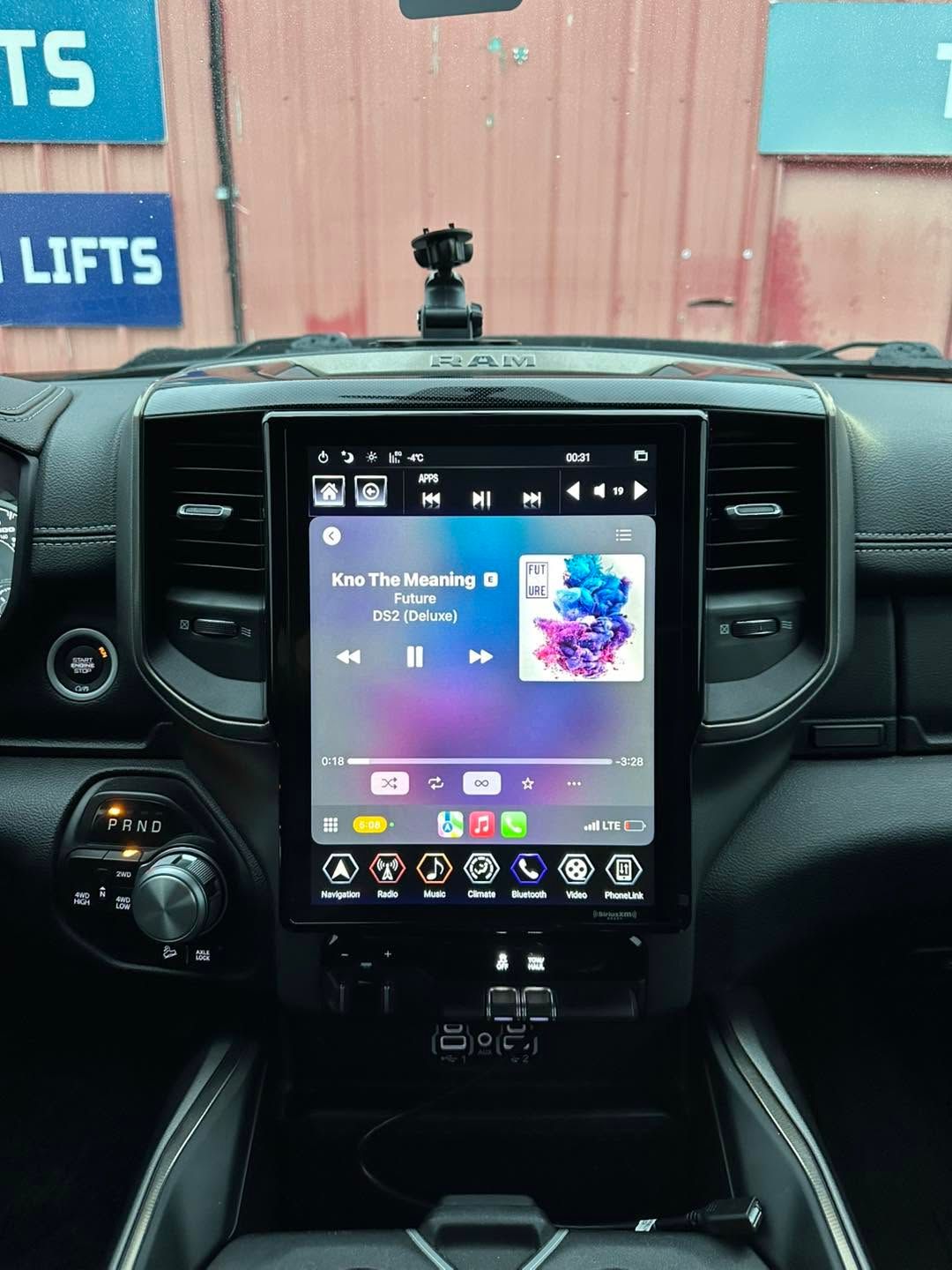 Car dashboard with a large central touchscreen showing music playback controls and app icons.