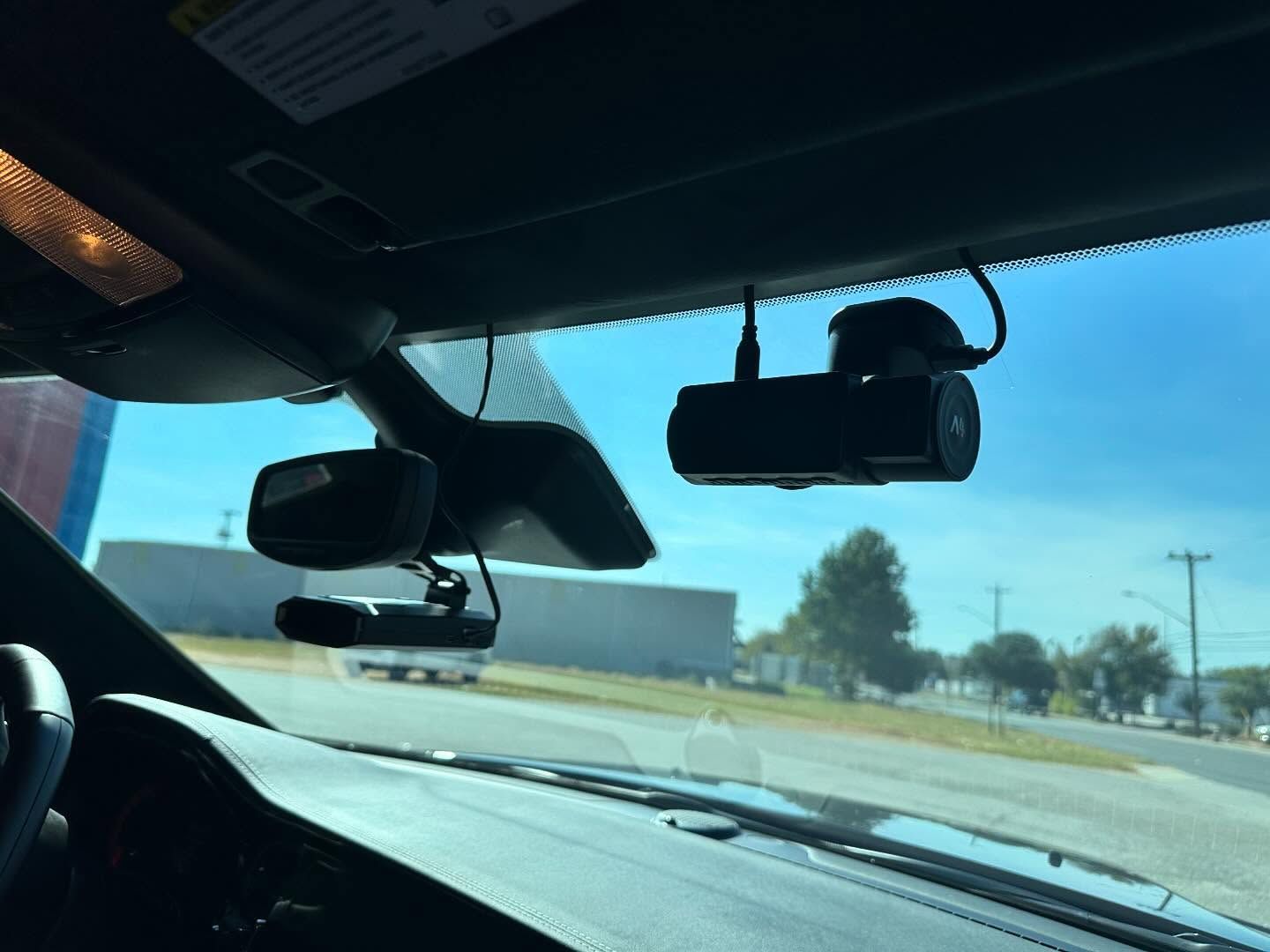 View through a car windshield on a sunny road, with dashcam and rearview mirror visible inside the vehicle