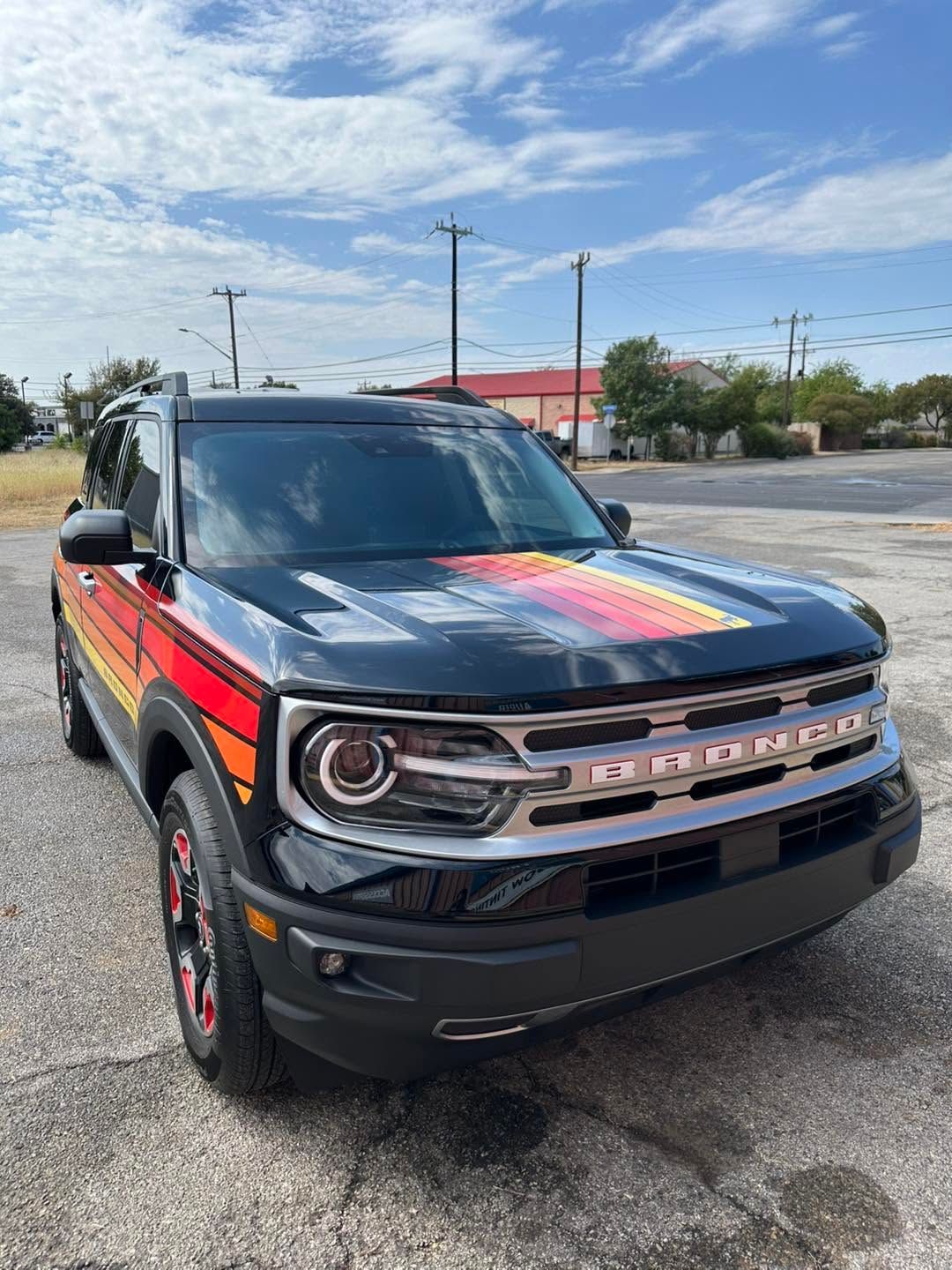 Black Ford Bronco with colorful rainbow hood wrap parked outdoors on a sunny day.
