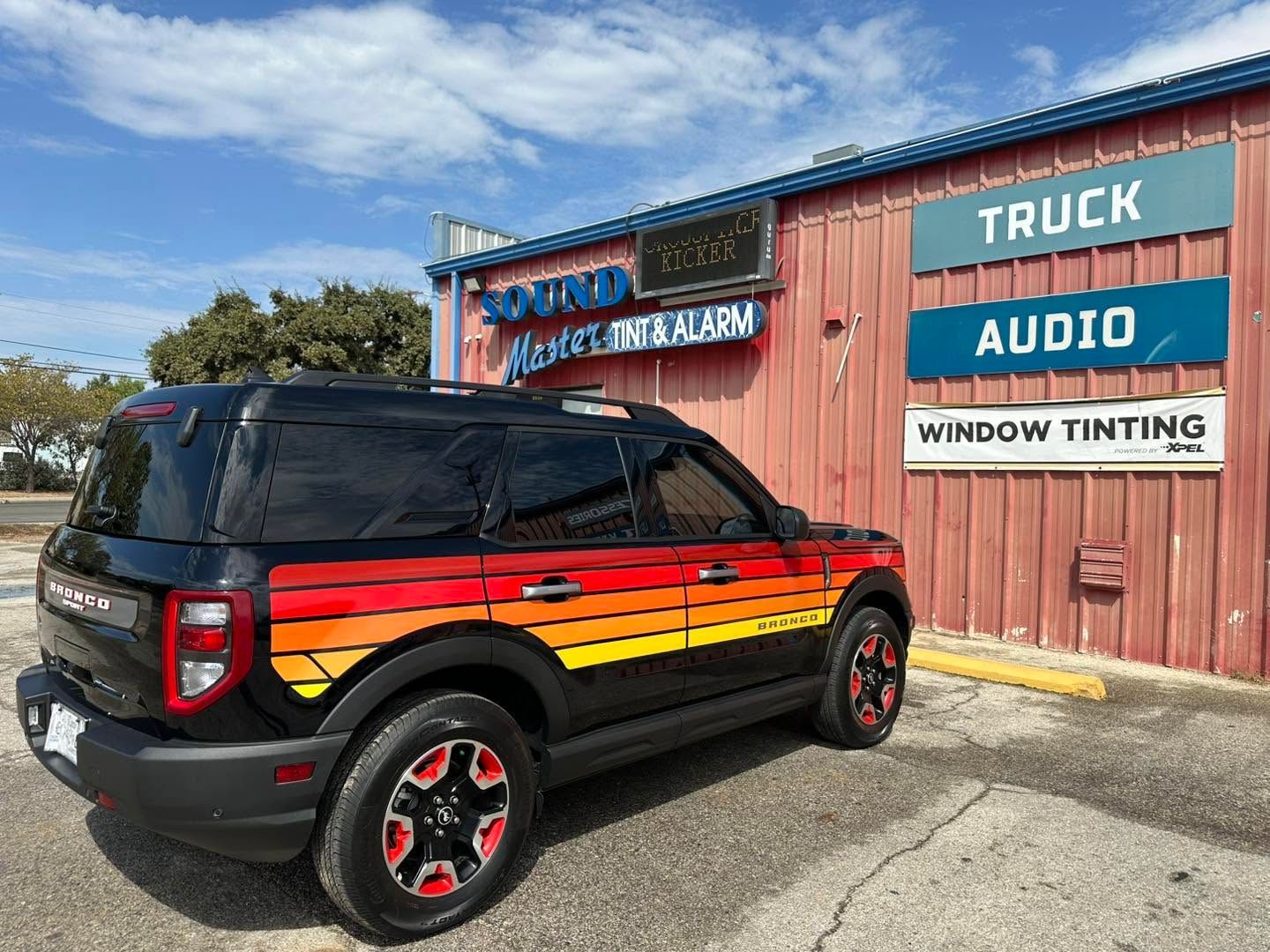 Black SUV with red-yellow flame decals parked by a truck audio and window tinting shop