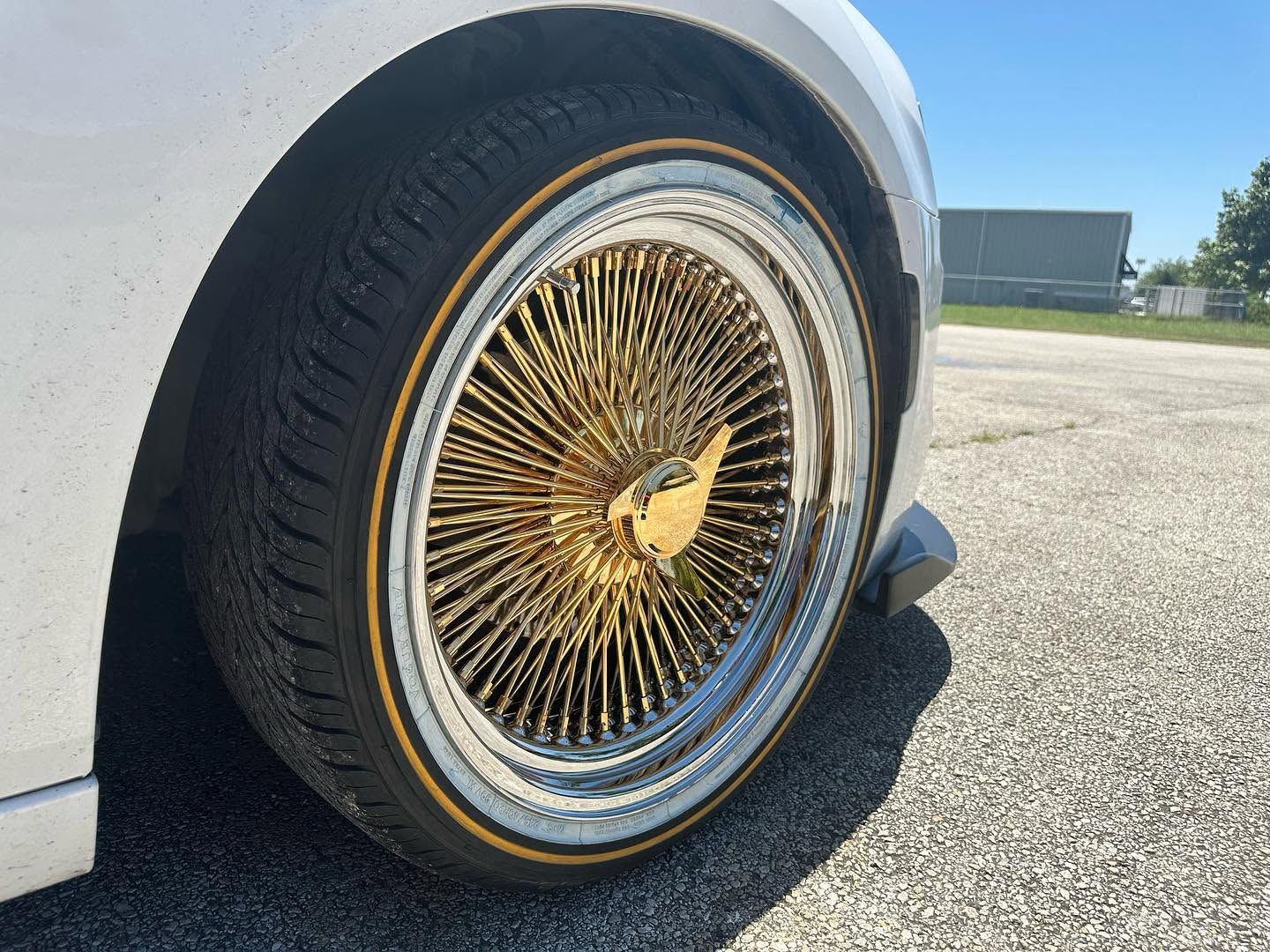 Close-up of a white car with gold wire-spoke wheel parked on pavement.