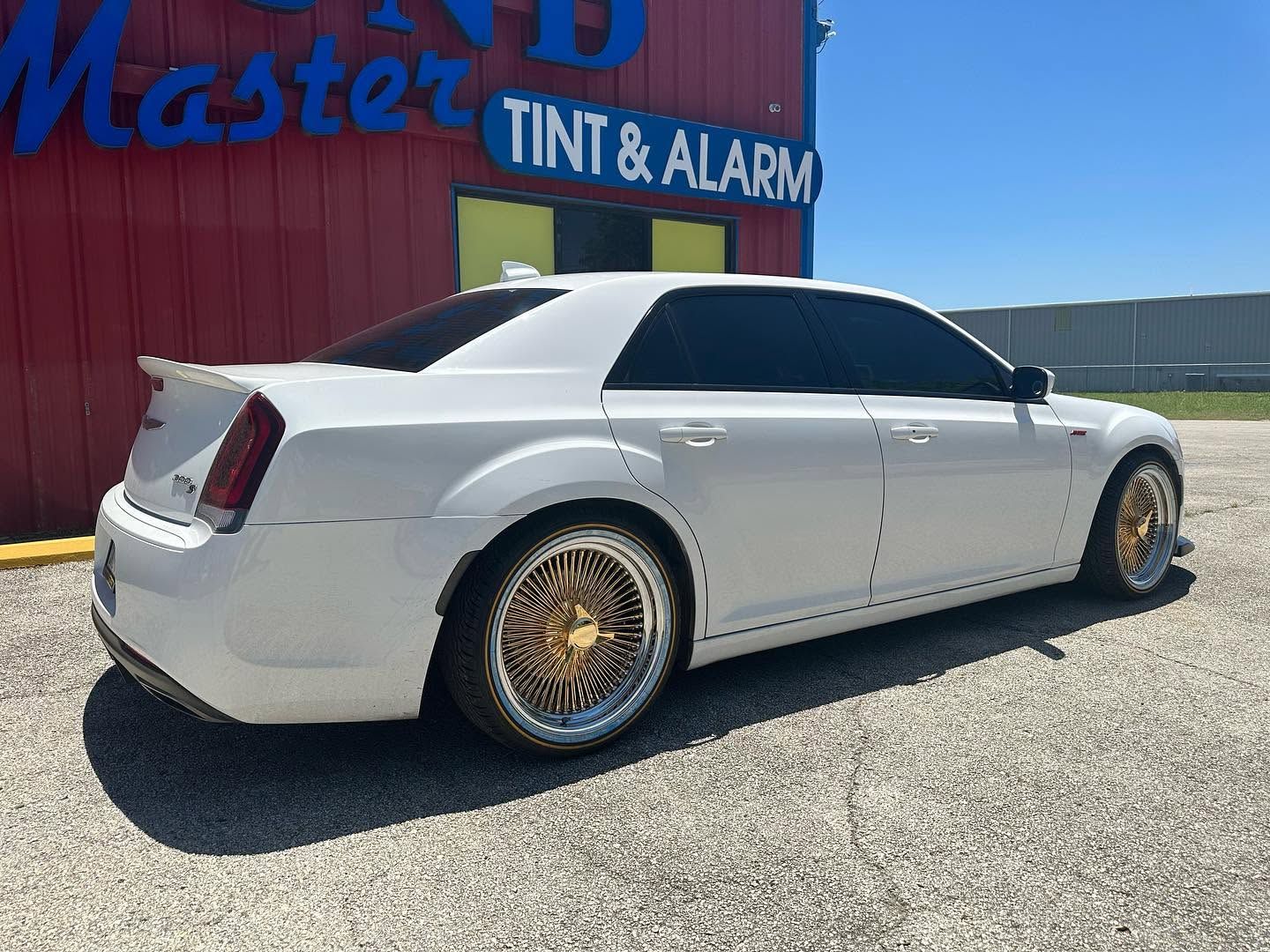 White sedan with tinted windows and gold rims parked outside a tint and alarm shop