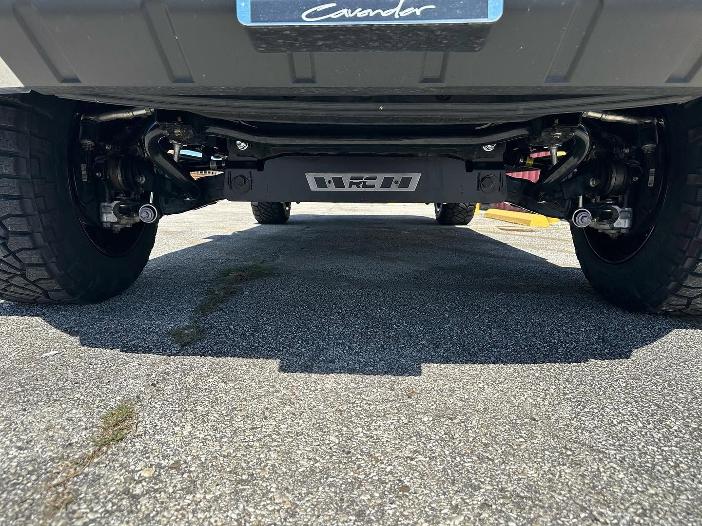 Underbody view of a vehicle on a gravel surface, showing suspension and rear axle.