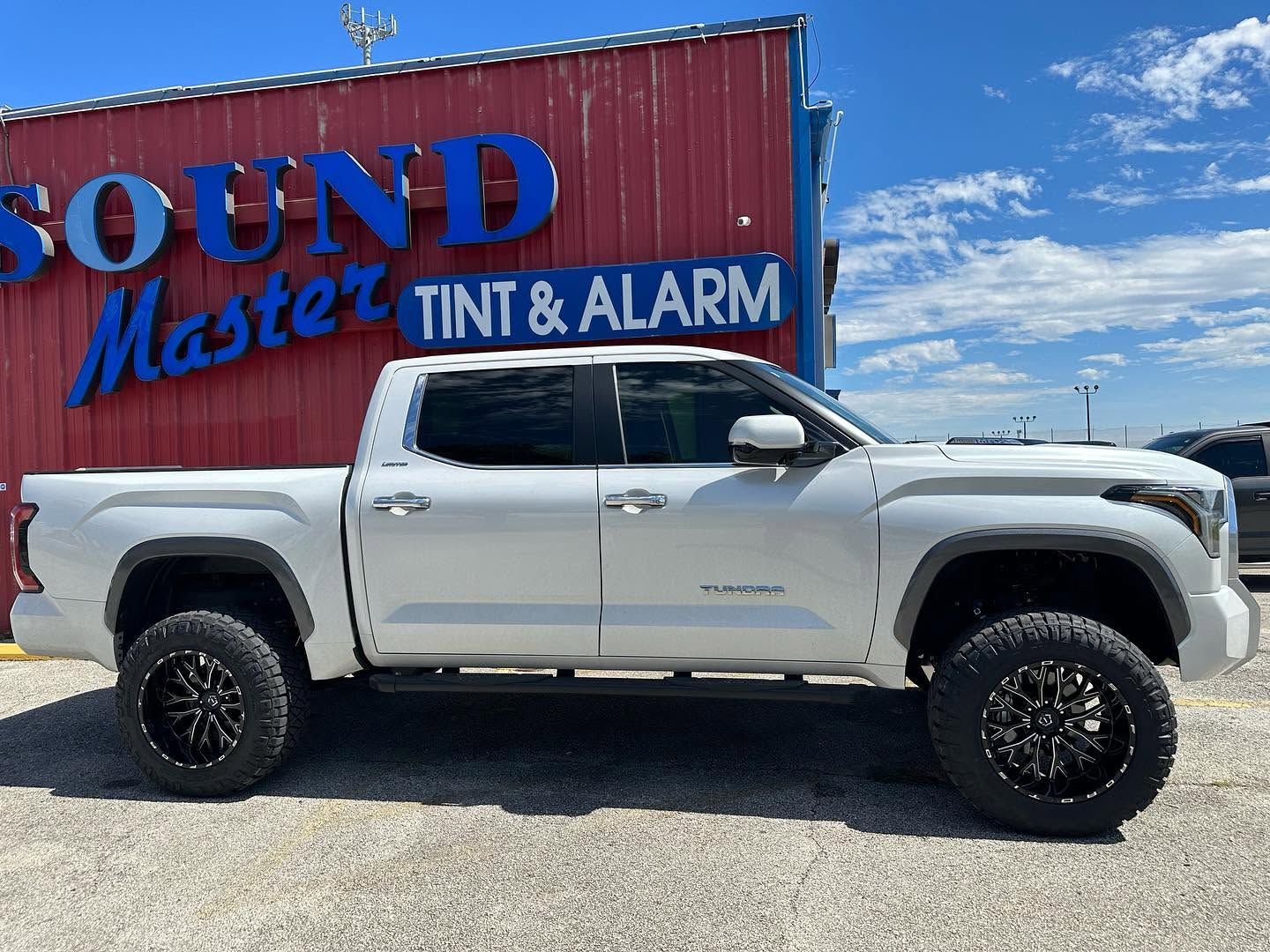 Silver pickup truck parked beside a red building with a blue “Sound Master Tint & Alarm” sign.