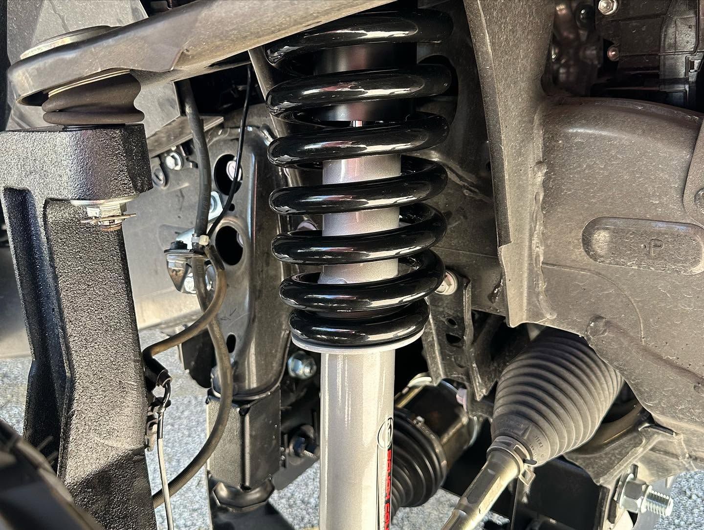 Close-up of a car suspension strut and coil spring with steering components visible.