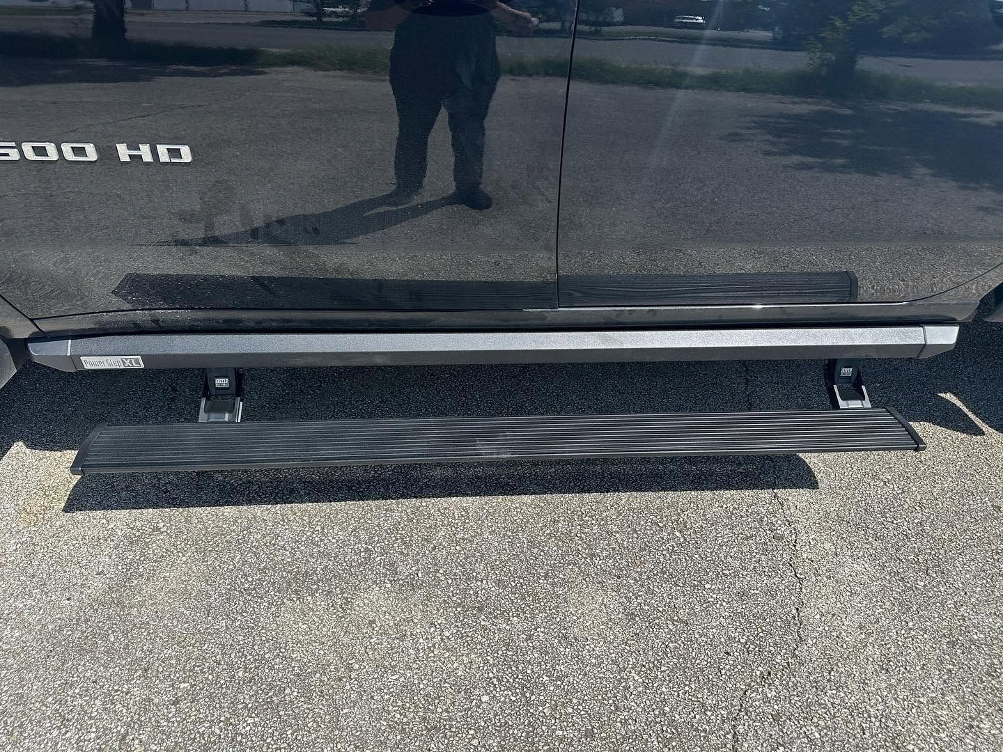 Black truck side step/nerf bar resting on asphalt beside a vehicle door.