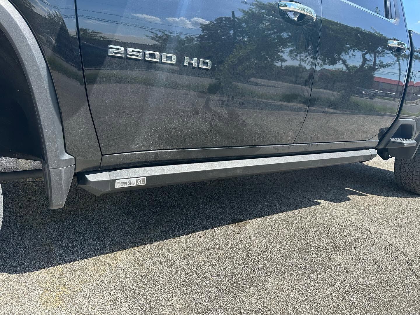 Side view of a dark gray Ram 2500 HD pickup truck on a sunny street, showing the running board and front wheel.