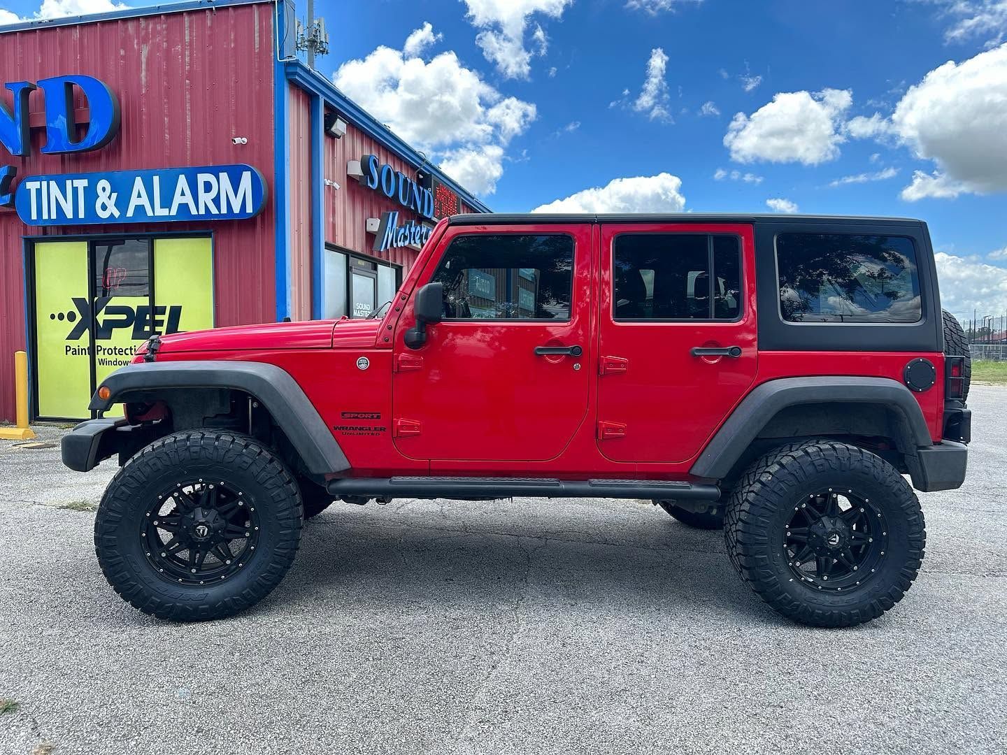 Red Jeep Wrangler parked outside a shop with a blue and red facade.