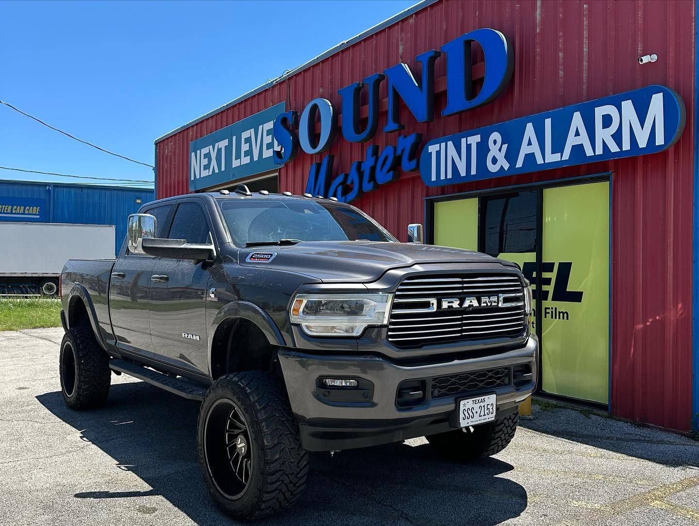 Lifted gray GMC pickup parked outside Next Level Sound and Tint & Alarm shop