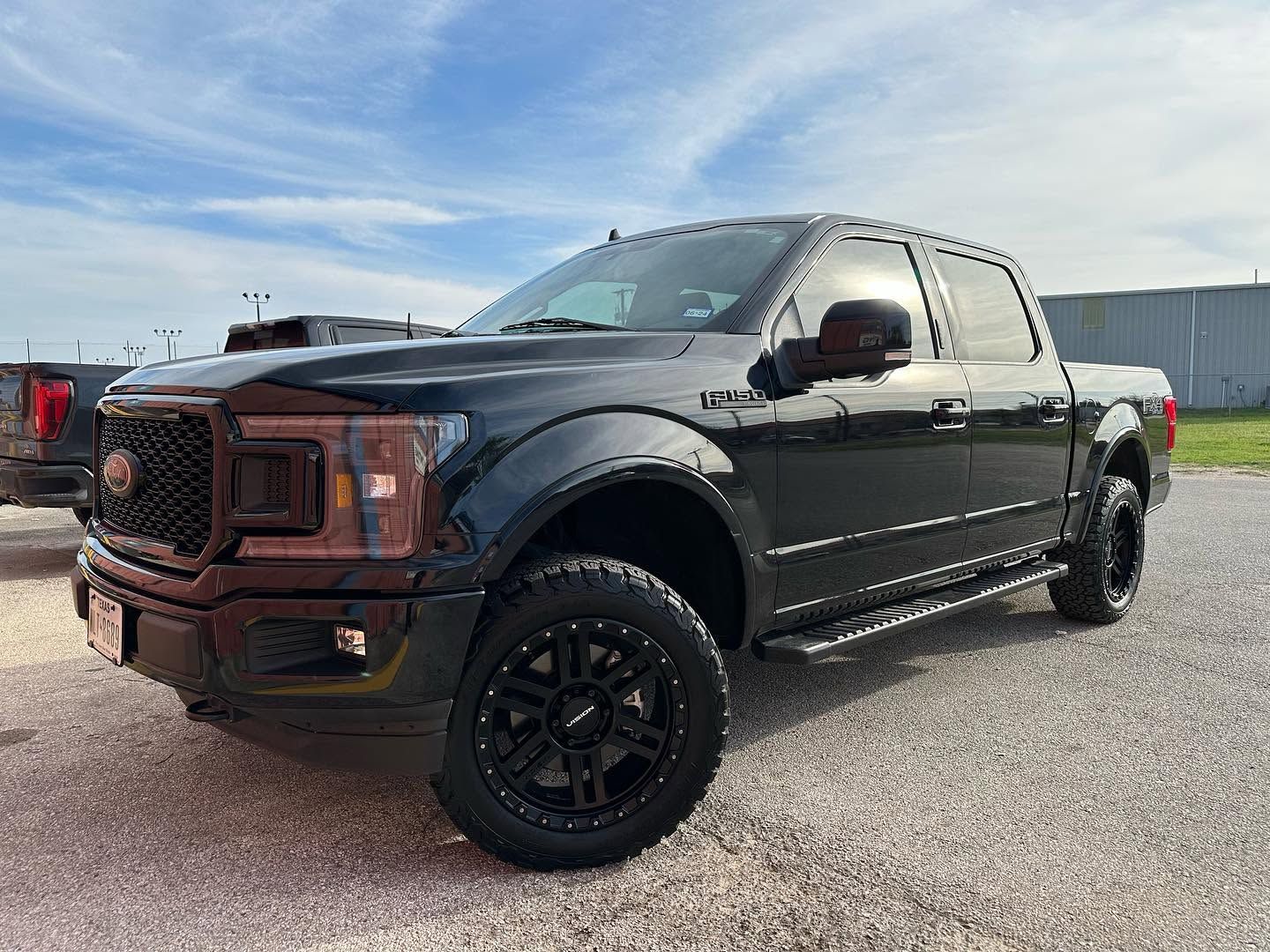 Black lifted pickup truck with tinted windows and off-road tires parked on gravel under a blue sky
