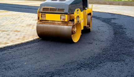A yellow steamroller compacts fresh, dark asphalt on a construction site.
