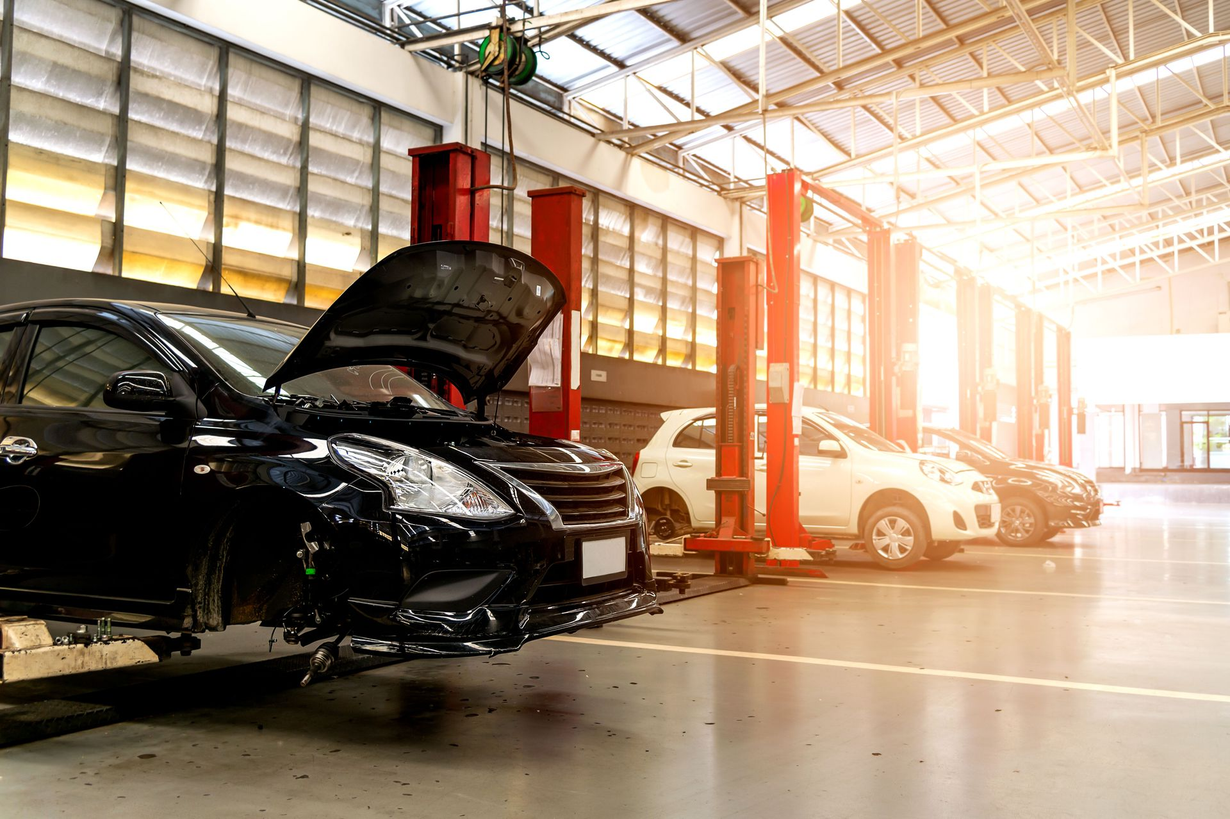 Cars in a bright auto repair shop, with one car's hood open near a lift.