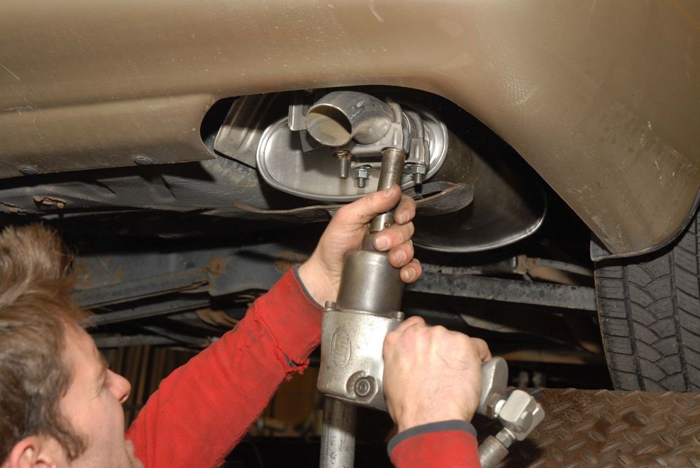 Mechanic using a socket wrench under a car to work on the exhaust system