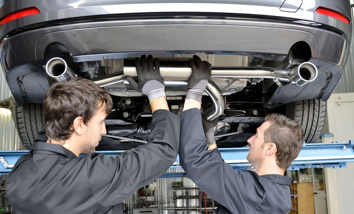 Two mechanics inspecting the underside of a car on a lift in a repair shop