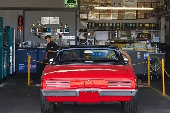 Red vintage convertible at a diner counter with a person behind it and a worker inside the shop