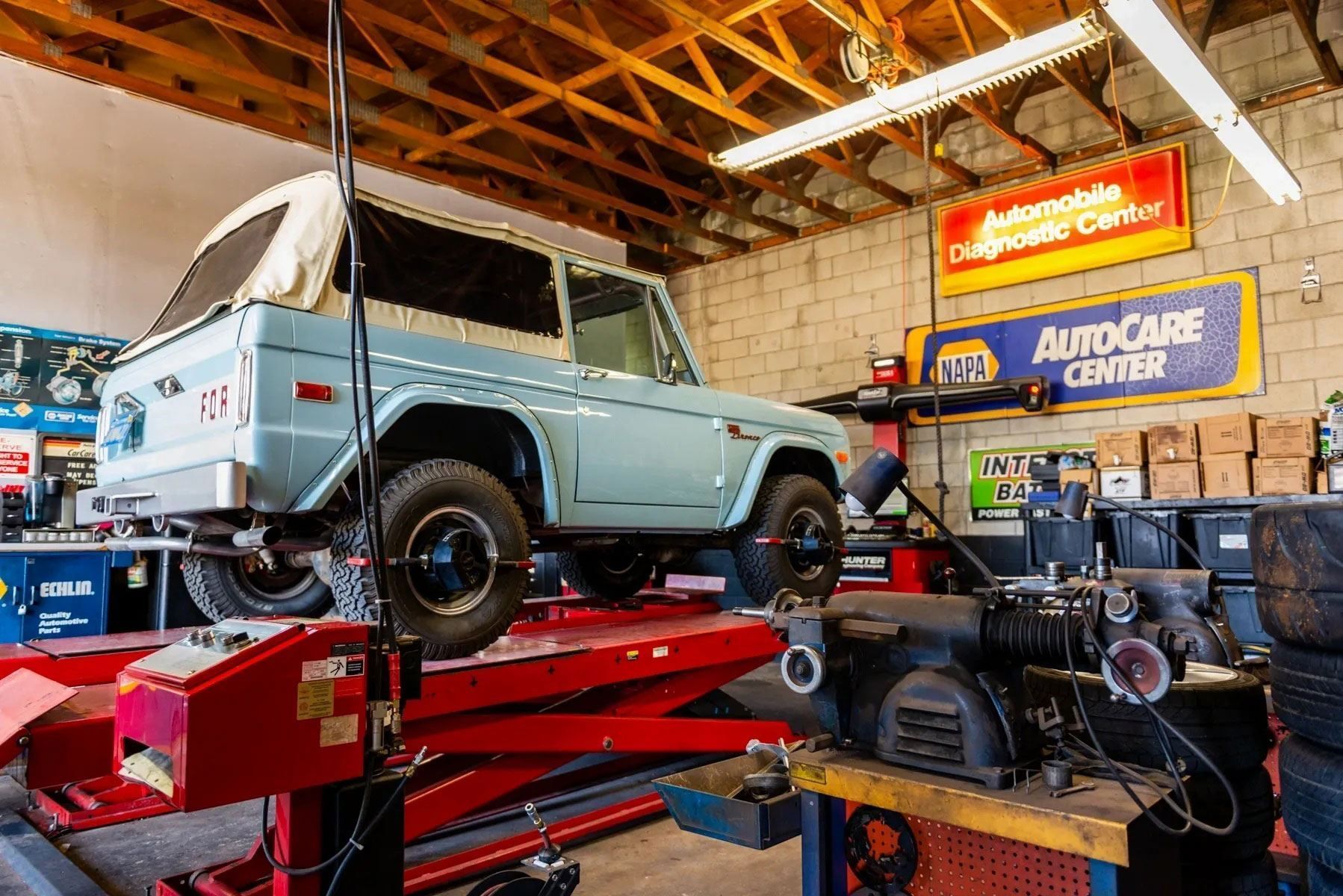 Classic blue SUV on a red lift in an auto repair garage with tools and signs.