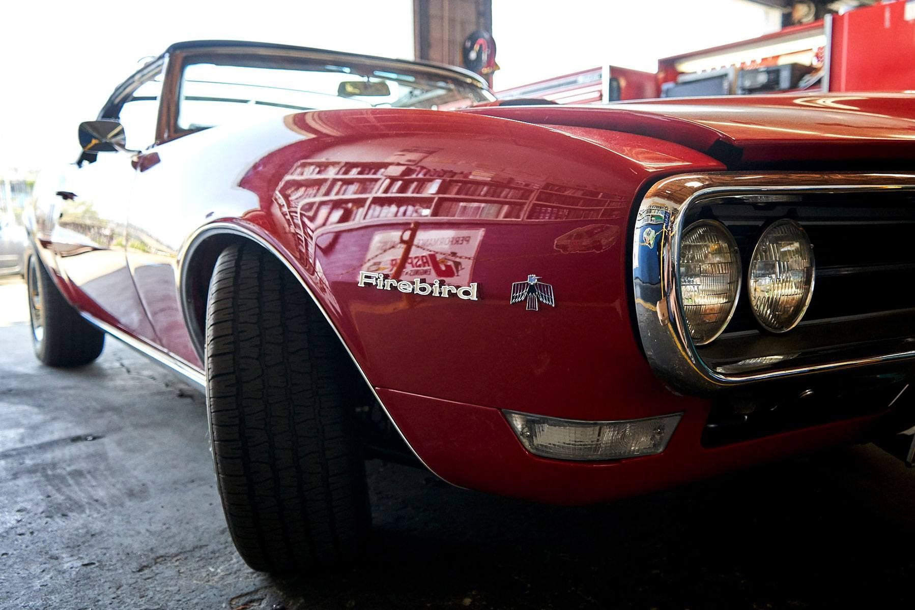 Red classic muscle car in a garage, front angle with chrome headlights and maroon paint